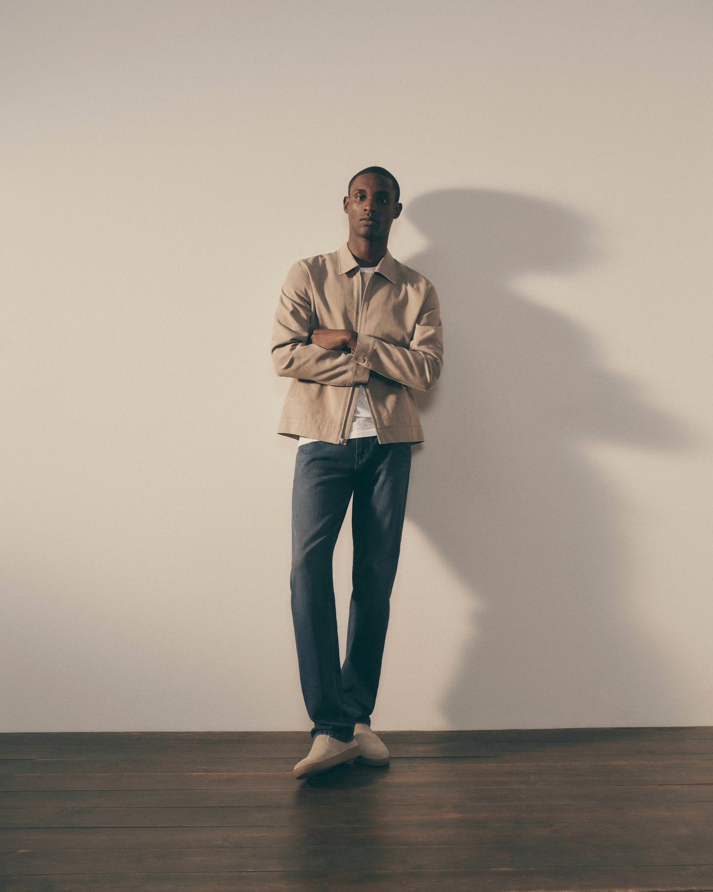 Man standing against a plain wall with a neutral expression