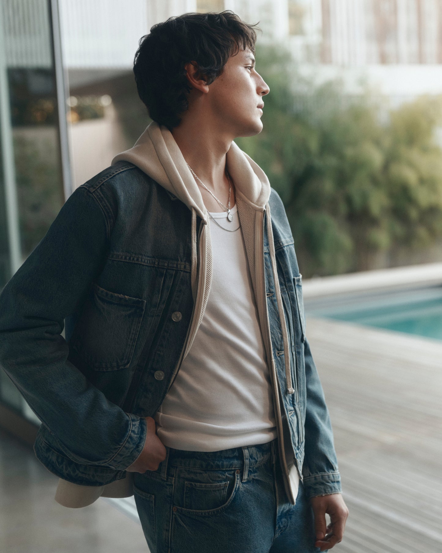 Person wearing a denim jacket and white shirt standing by a poolside.