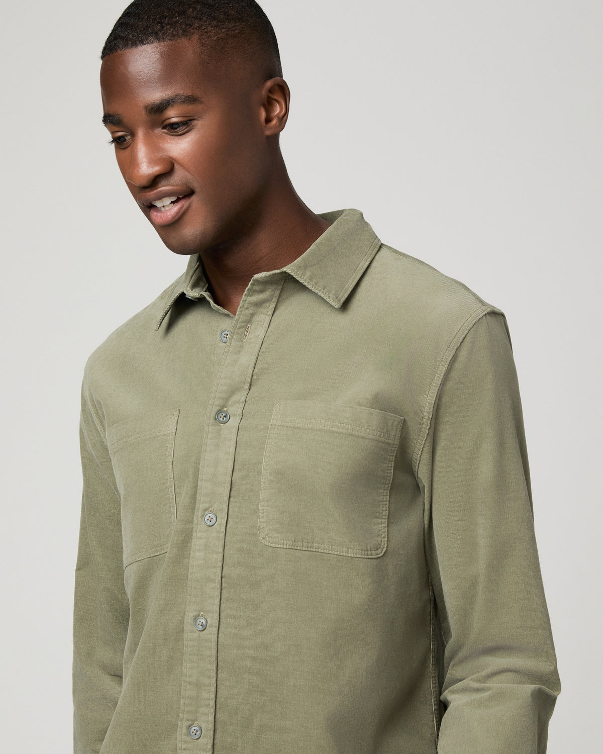 Close-up front view of a man in a sage green corduroy shirt, highlighting the fine-wale texture, chest pocket, and collar.