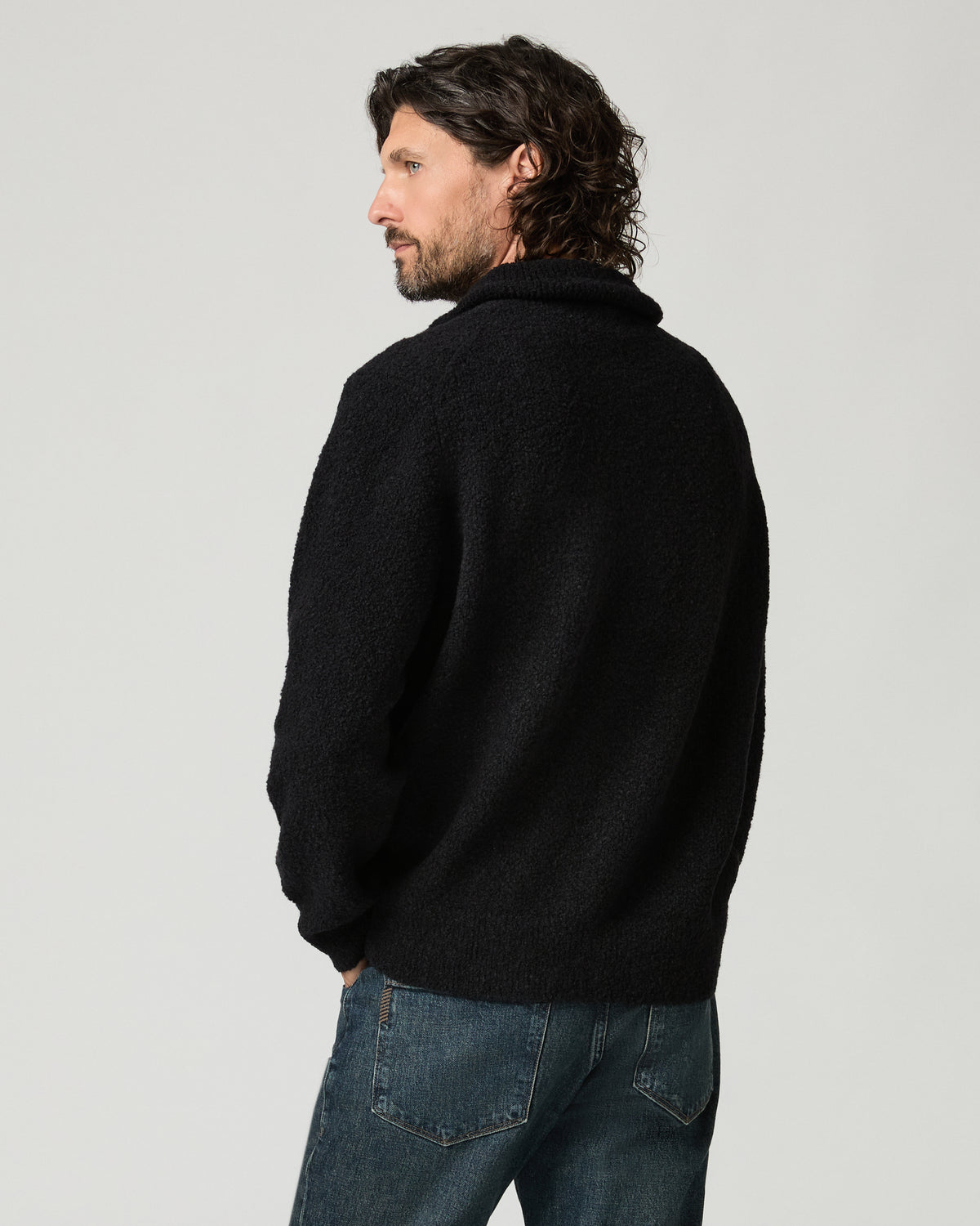 Back view of a man wearing the black bouclé-knit Donover Quarter Zip Sweater, highlighting the funnel collar and textured knit, paired with faded blue jeans.