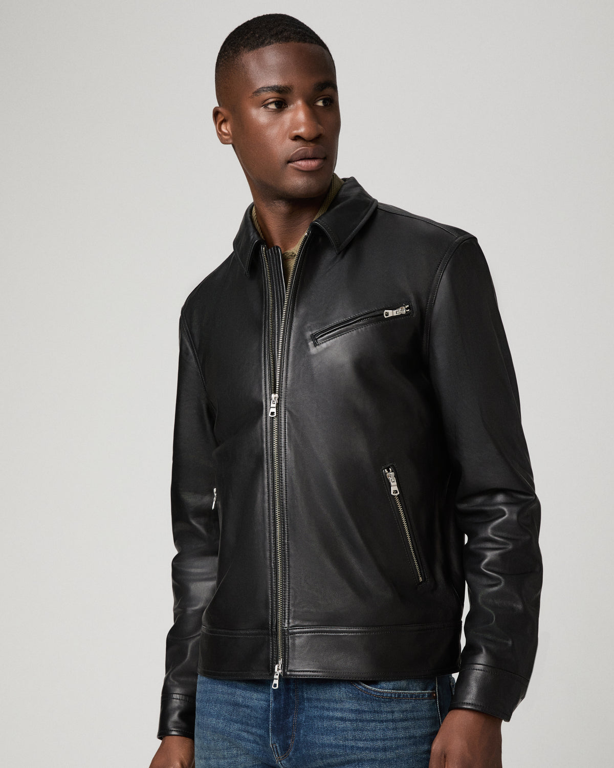 Close-up view of a man wearing the black leather Rocoso Moto Jacket, showing the silver-tone zip pockets and point collar over an olive shirt.