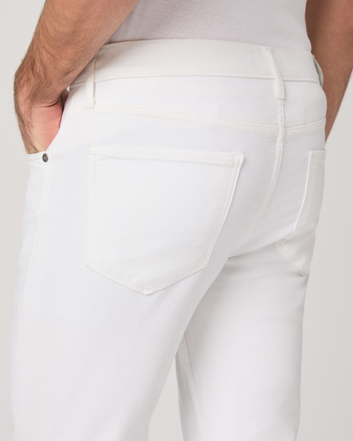 Man wearing a white shirt and white pants on a plain background