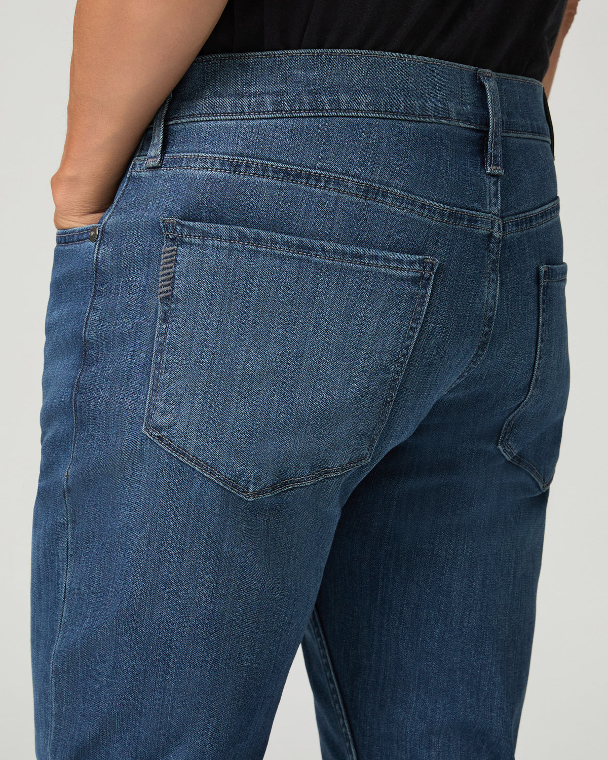 Close-up back view of medium blue slim-fit jean pockets, showing a leather brand patch, contrast stitching, and fading detail.
