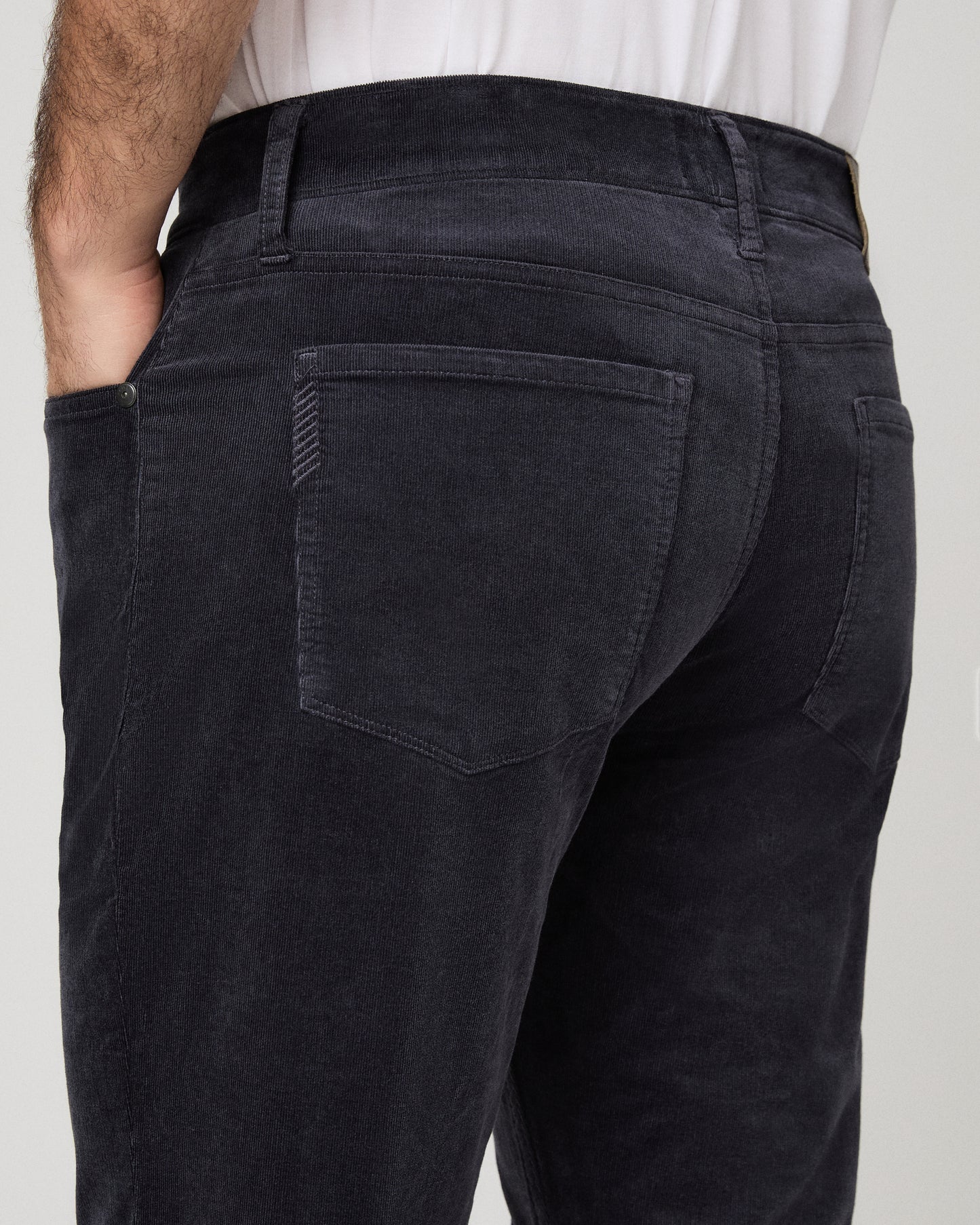 Close-up back view of a person wearing dark charcoal corduroy trousers, showing the back pocket detail and waistband.