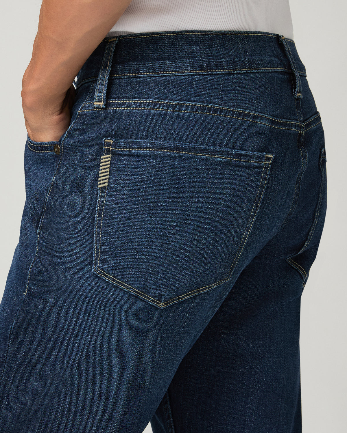 Close-up back pocket detail of deep blue slim-straight jeans, showing a leather brand patch and contrast stitching.