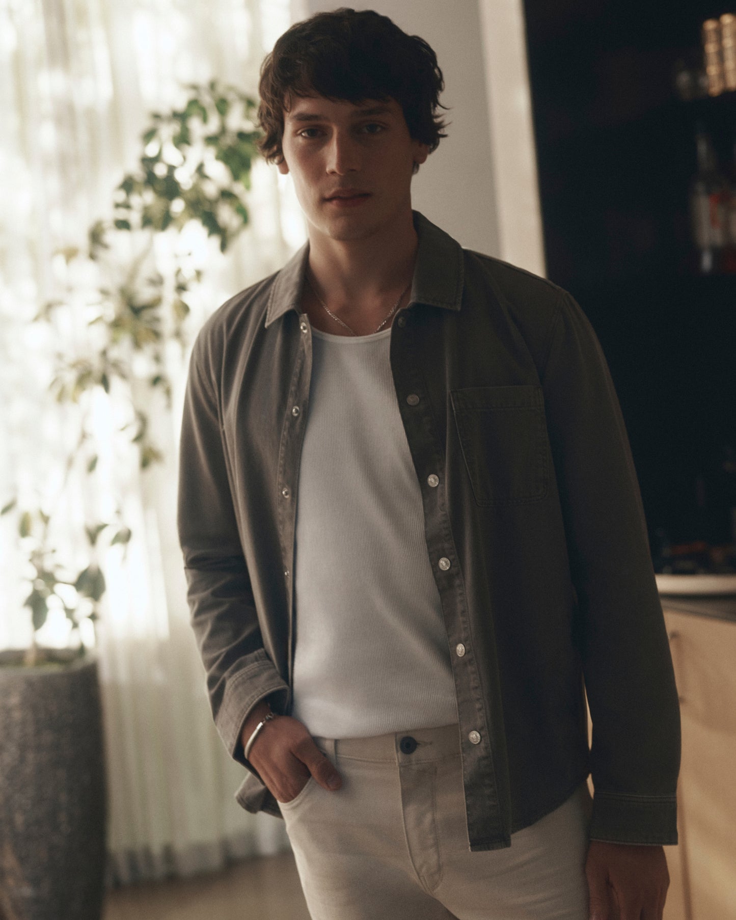 Man wearing a dark jacket over a white shirt and light pants indoors.