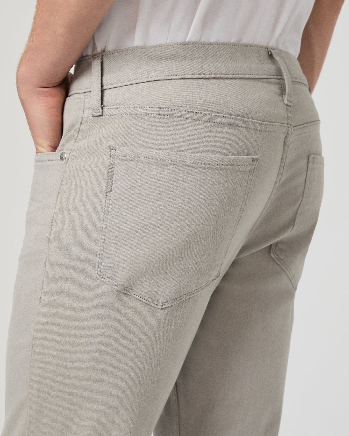 Man wearing a white shirt and grey jeans on a light gray background