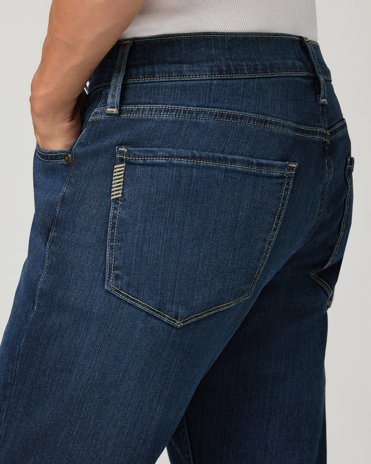 Extreme close-up of the back pocket on deep blue slim-straight jeans, showing a woven brand tab and contrast stitching.