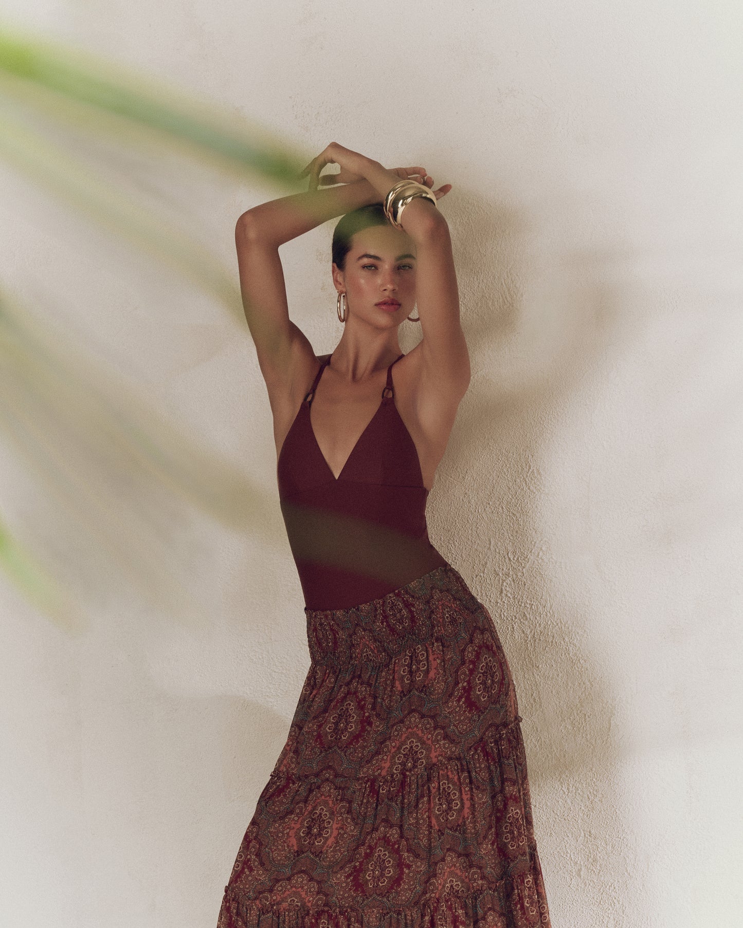 Woman in a burgundy top and patterned skirt against a textured wall.