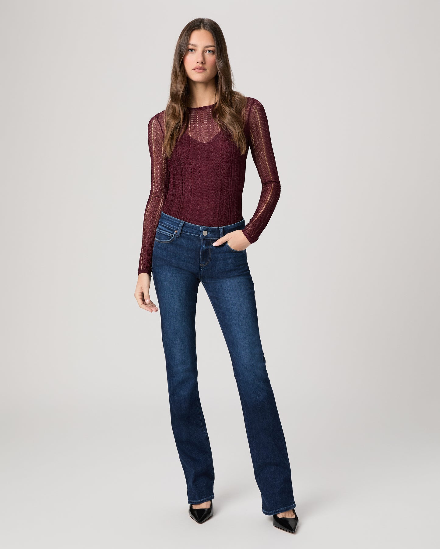 Woman wearing a burgundy top and blue jeans on a white background