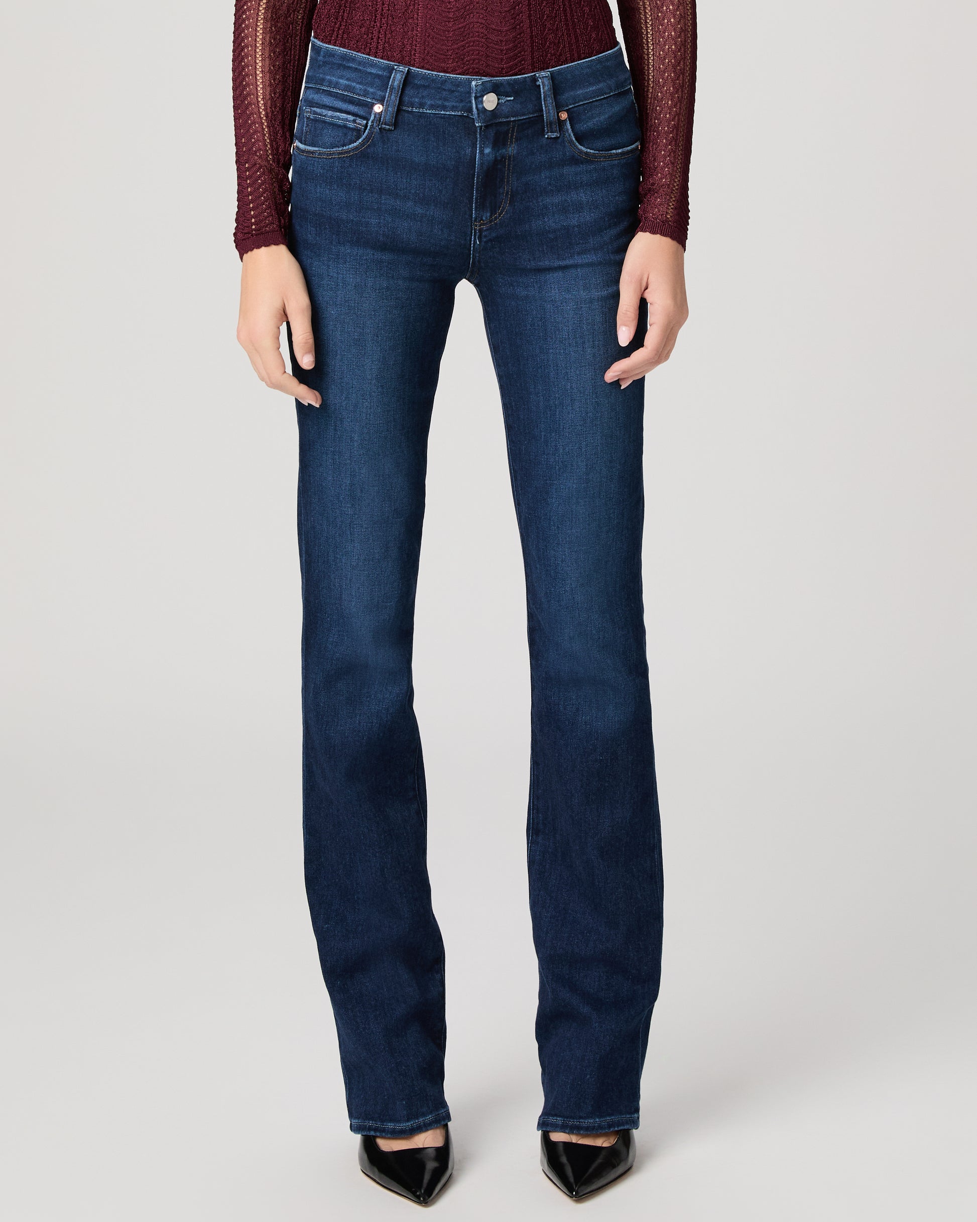 Woman wearing a burgundy top and blue jeans on a white background