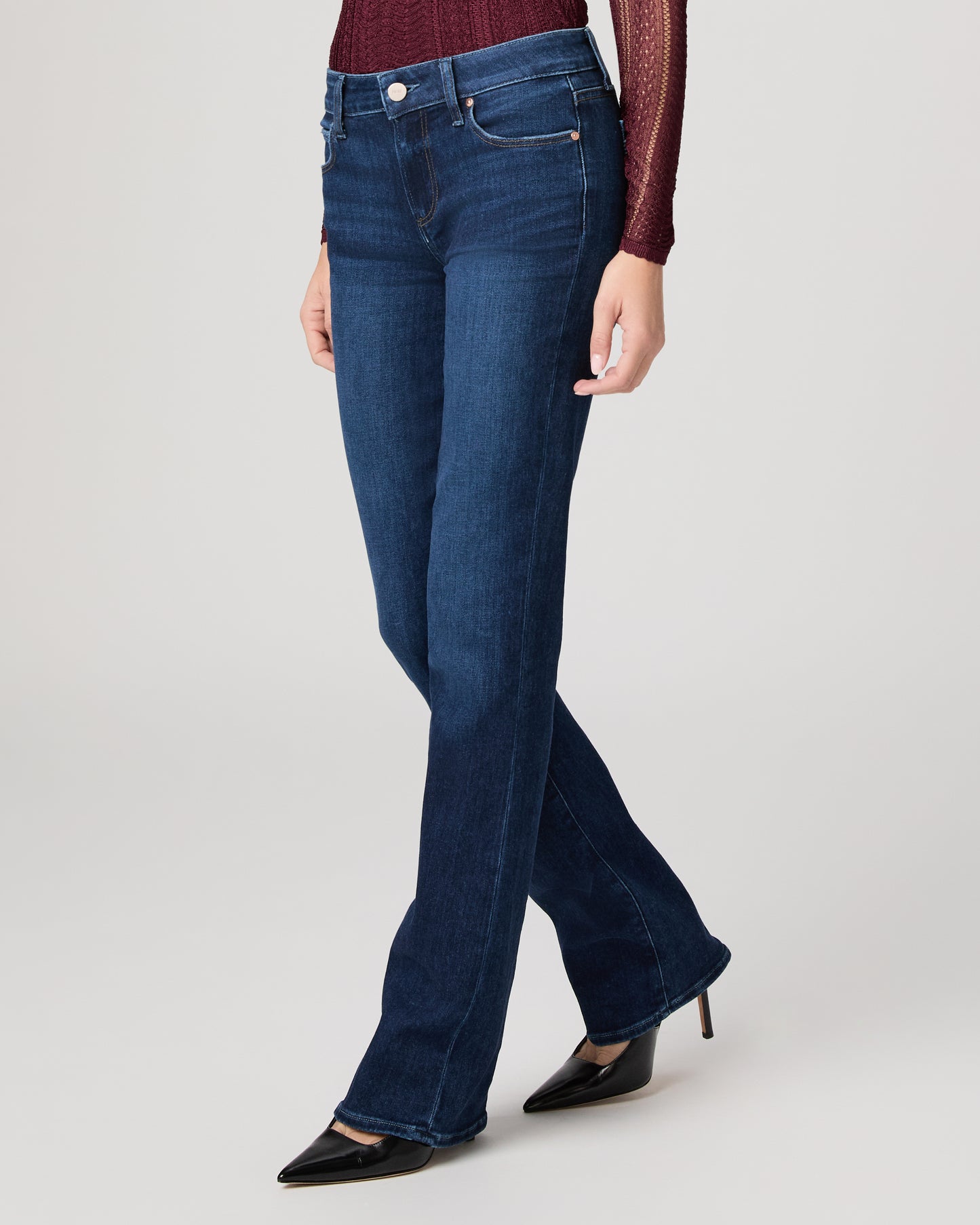 Woman wearing a burgundy top and blue jeans on a white background