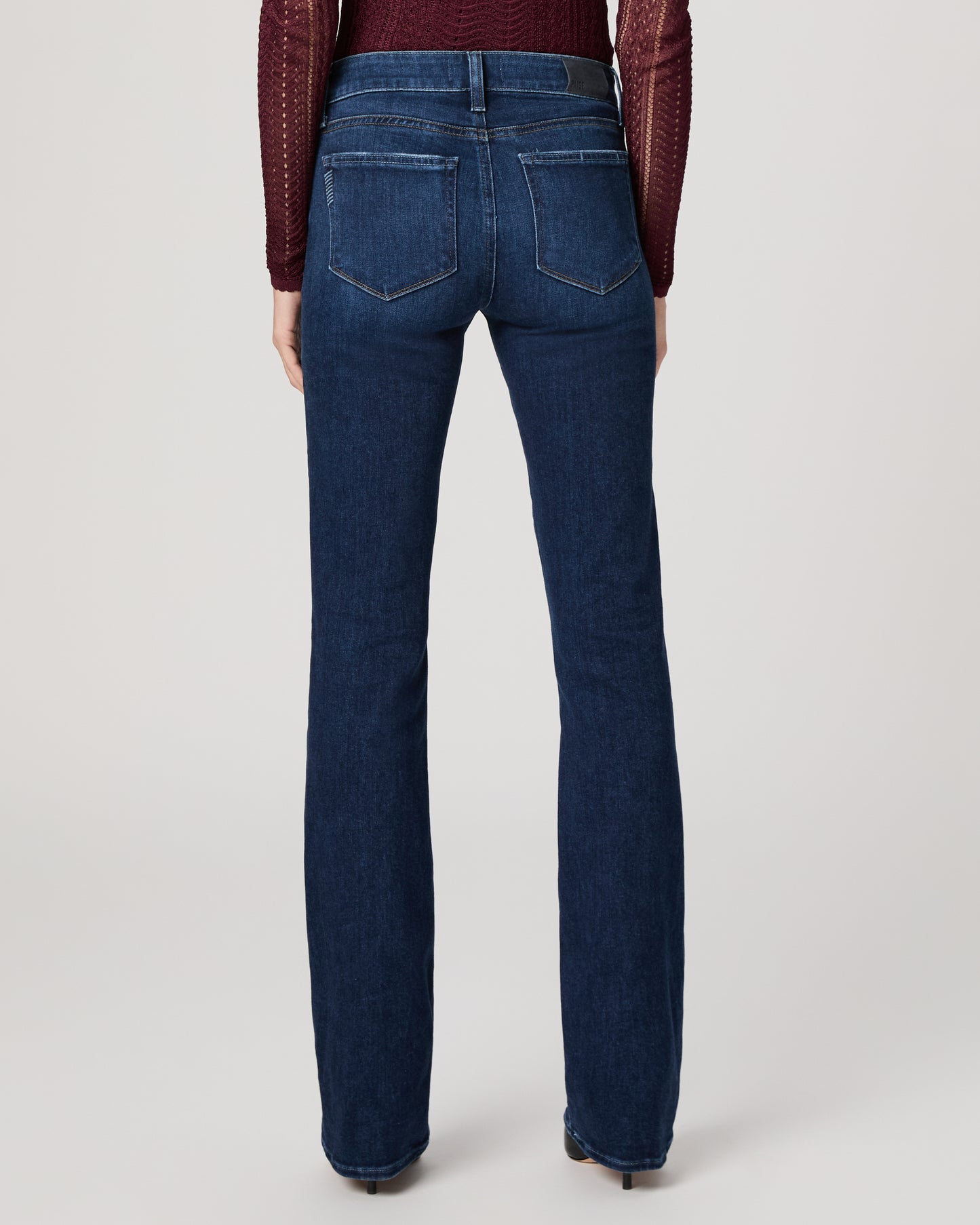 Woman wearing a burgundy top and blue jeans on a white background