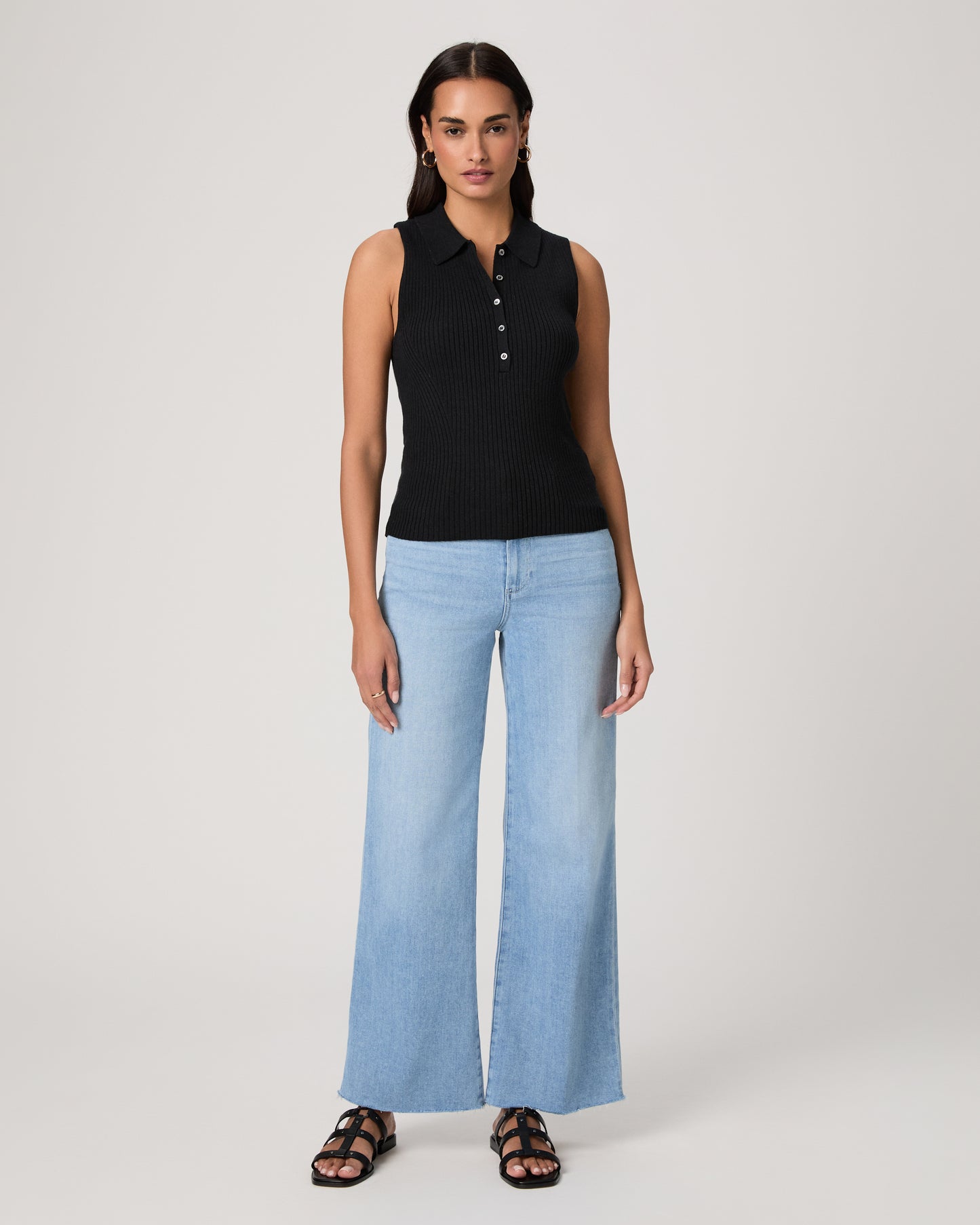 Woman wearing a black sleeveless top and light blue jeans on a white background