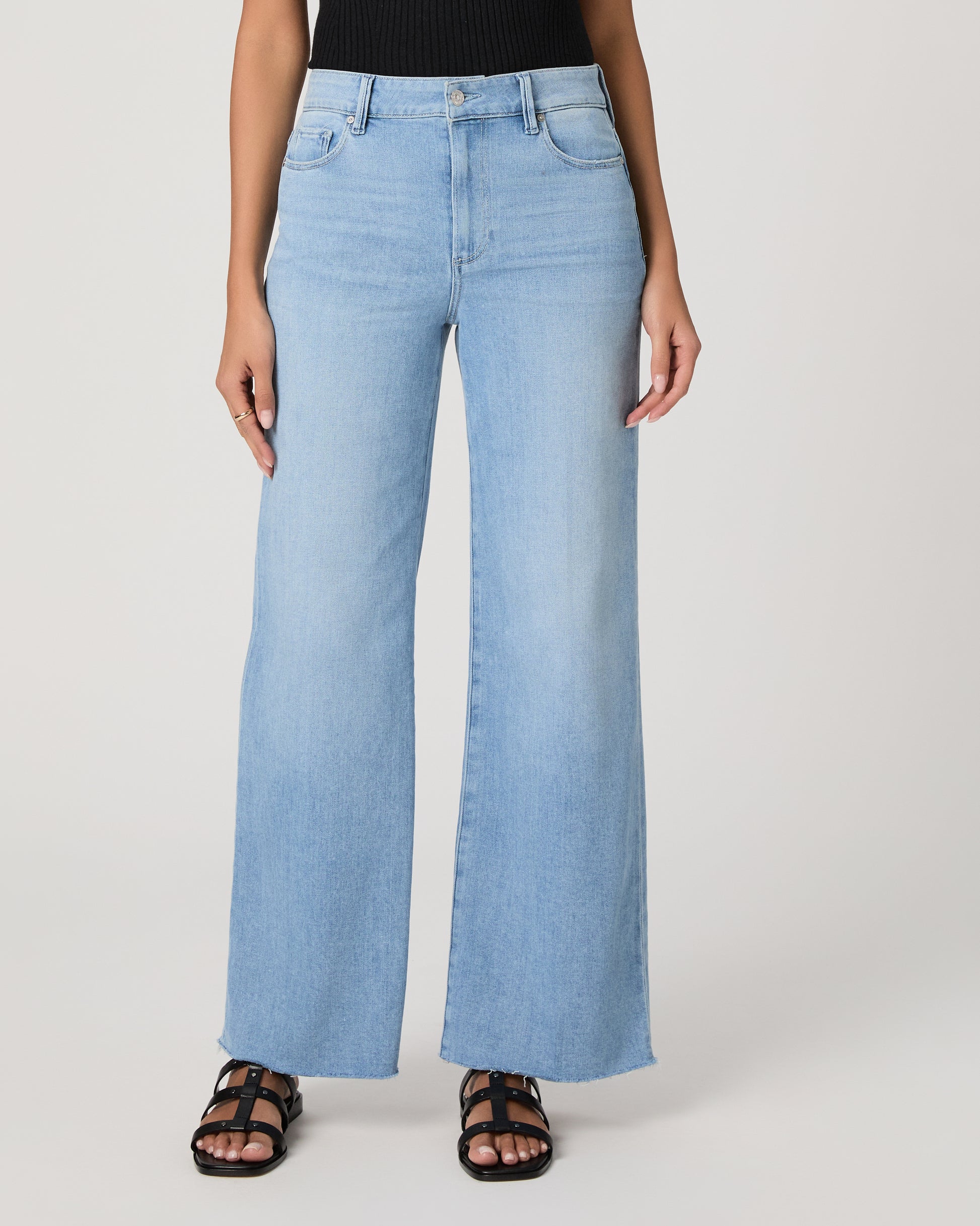 Woman wearing a black sleeveless top and light blue jeans on a white background