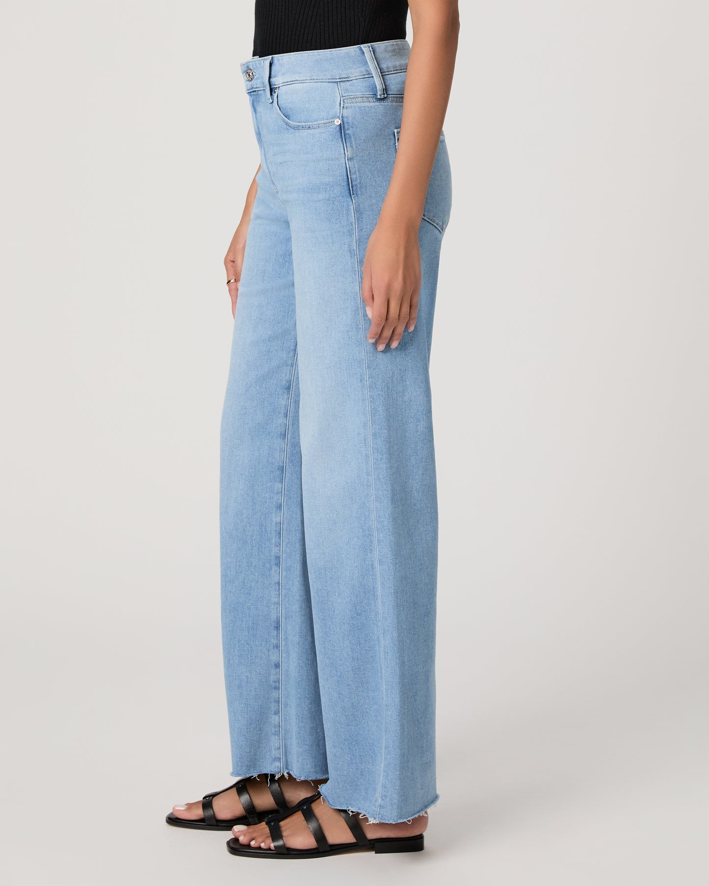 Woman wearing a black sleeveless top and light blue jeans on a white background