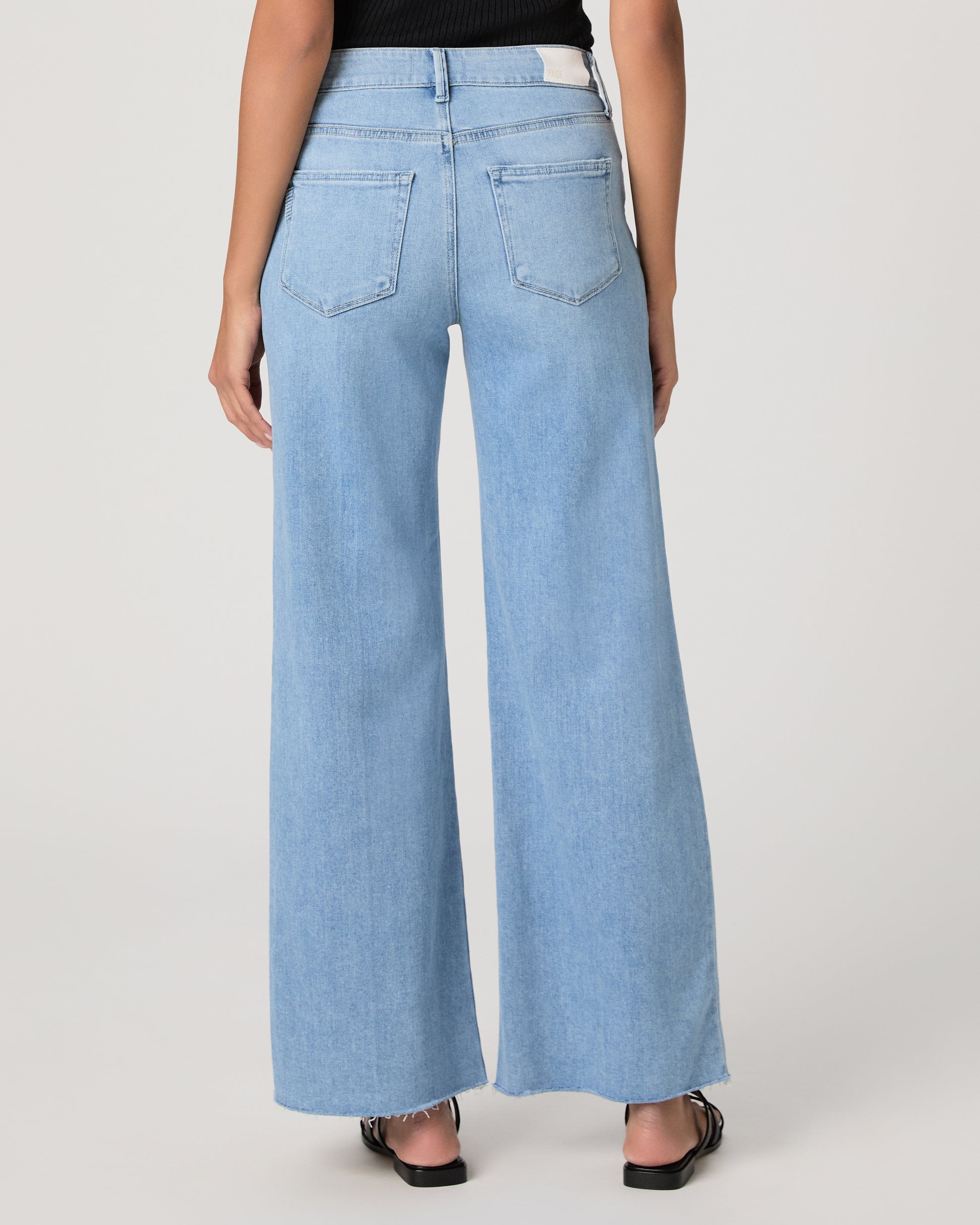 Woman wearing a black sleeveless top and light blue jeans on a white background