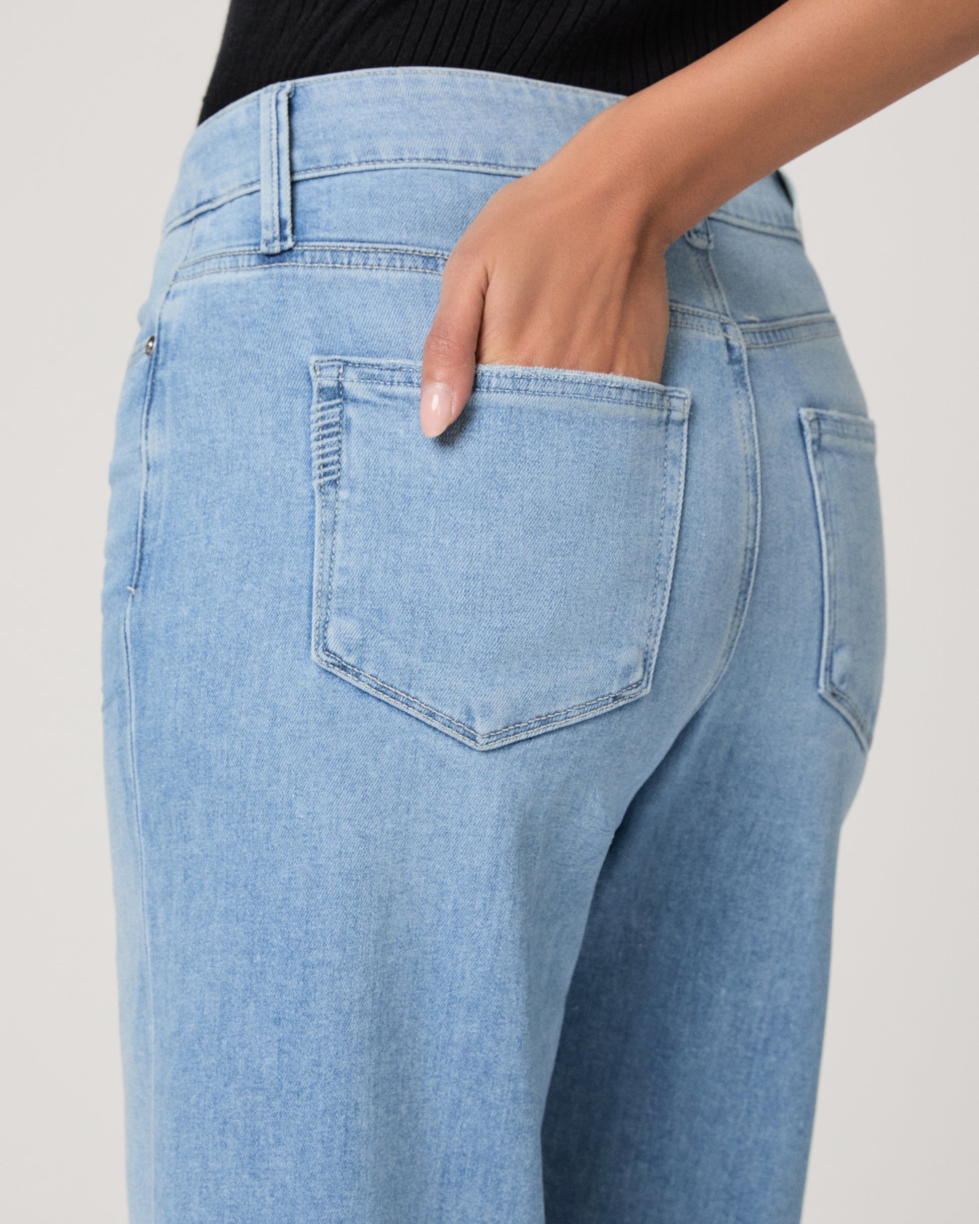 Woman wearing a black sleeveless top and light blue jeans on a white background