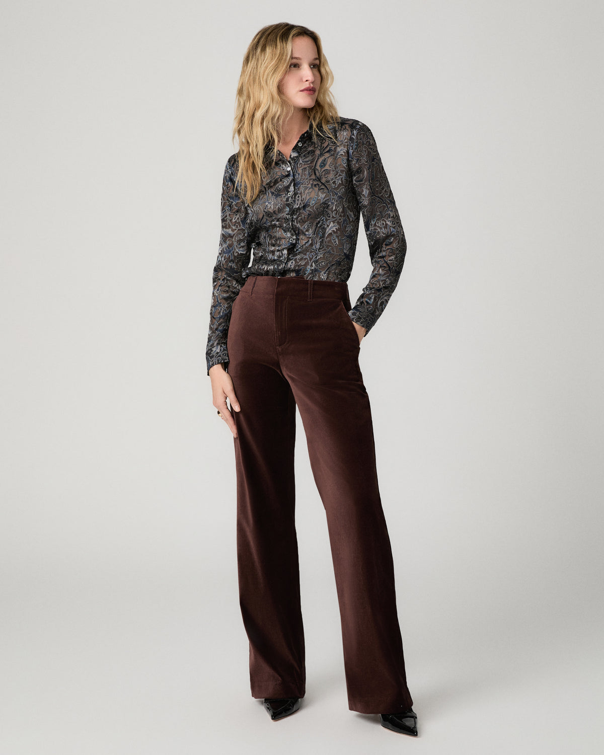 Women wearing a grey printed long sleeve top paired with suede burgundy jeans standing against a white background