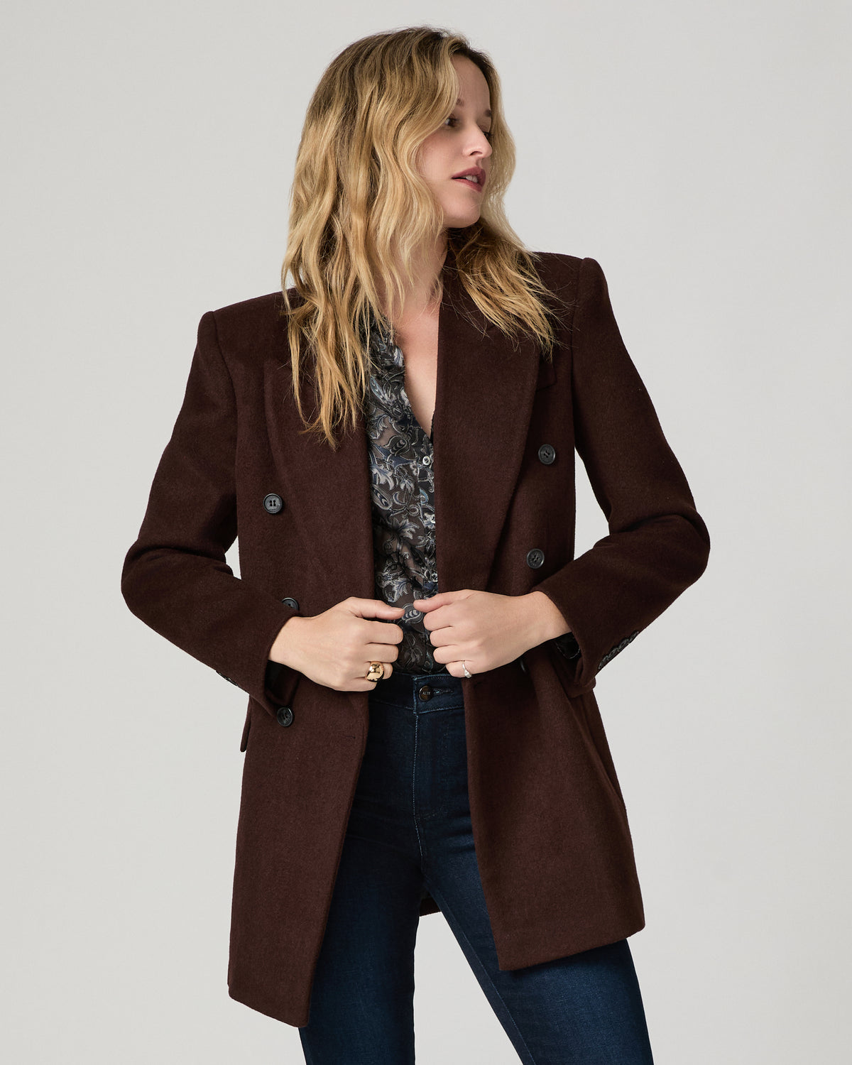 Women wearing a grey printed long sleeve top paired with burgundy blazer and blue jeans standing against a white background