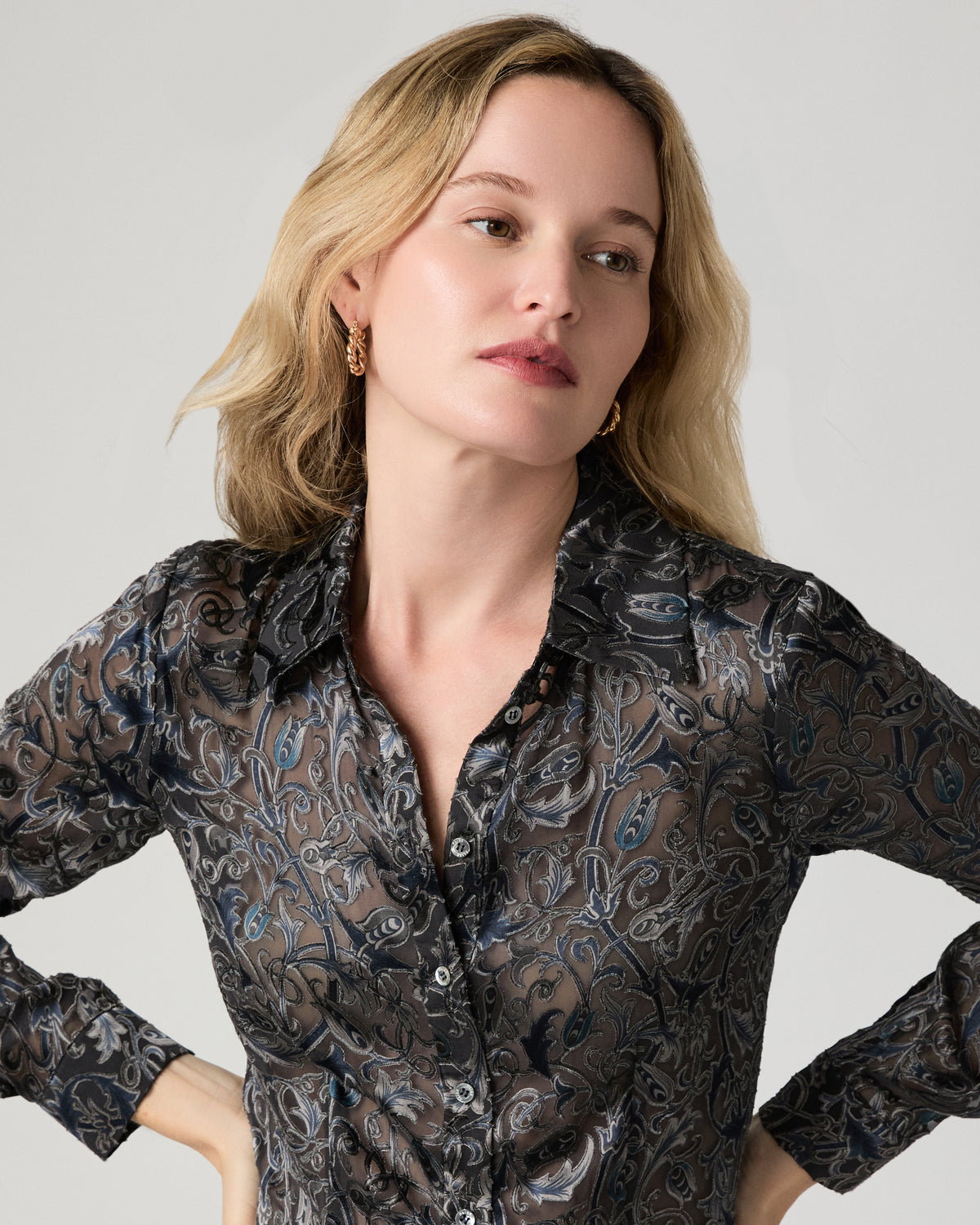 Women wearing a grey printed long sleeve top paired with suede burgundy jeans standing against a white background
