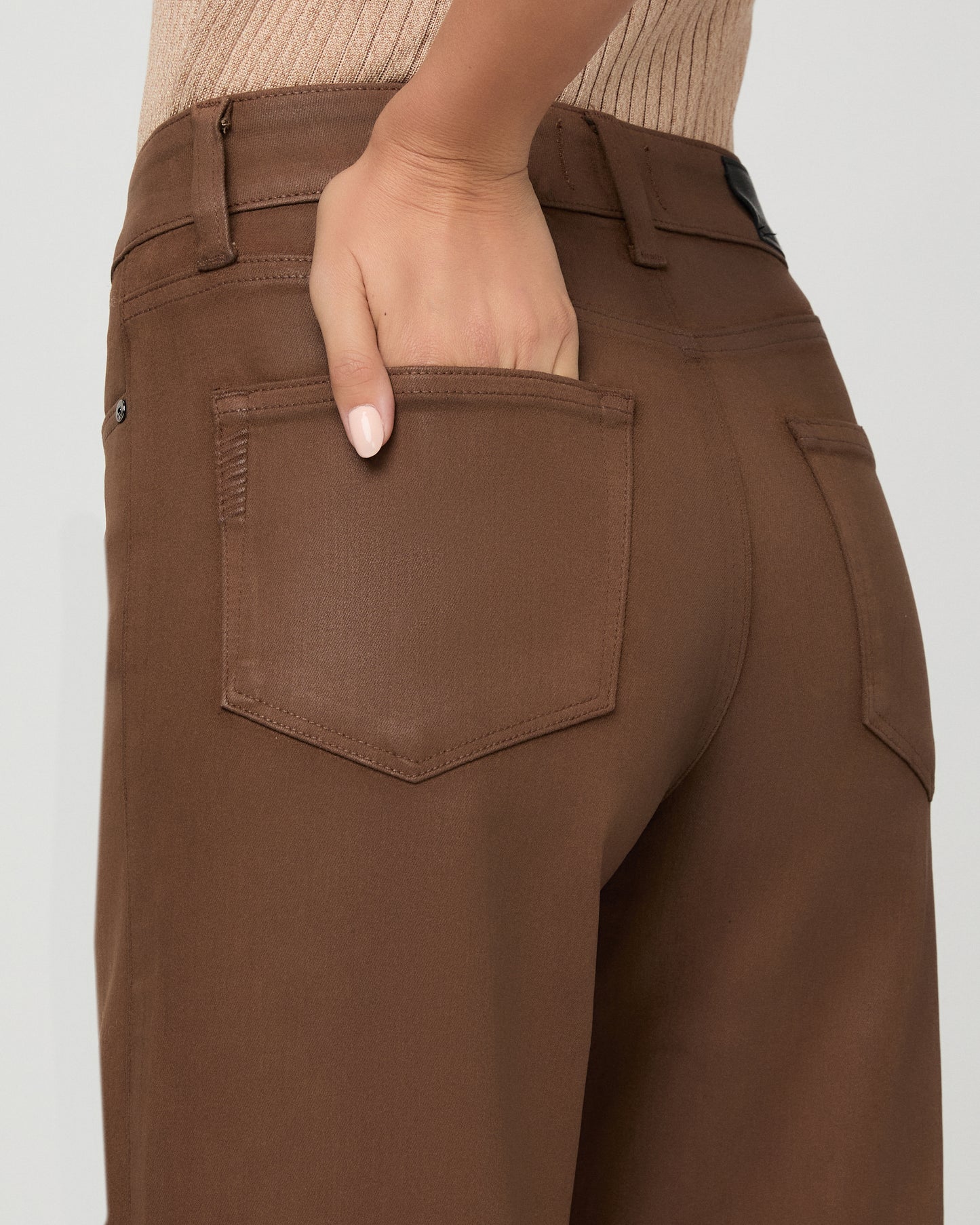A woman modeling a beige ribbed short-sleeve top and brown wide-leg pants against a light gray studio background.