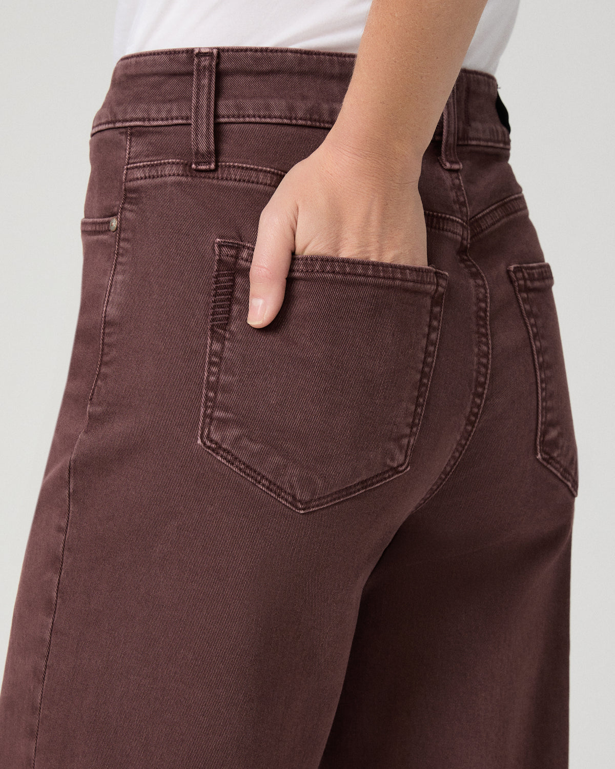 Women wearing a white top paired with burgundy jean and brown flats against a white background