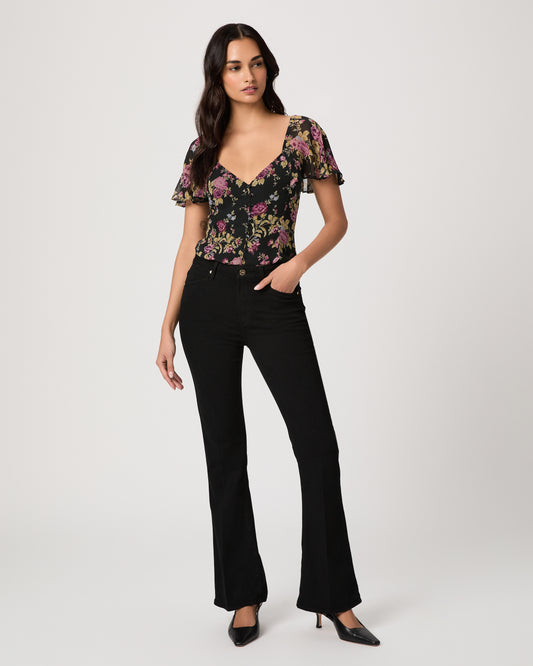 Woman wearing a floral to, black pants, and black heels on a white background