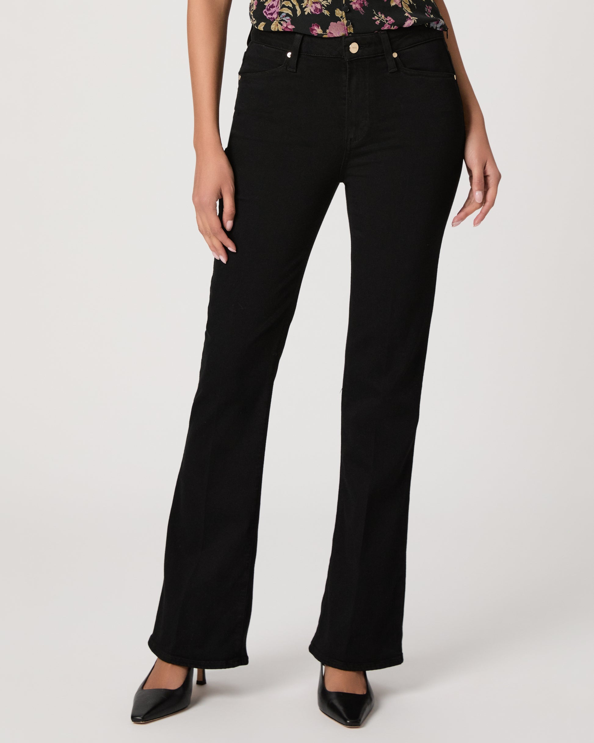 Woman wearing a floral to, black pants, and black heels on a white background