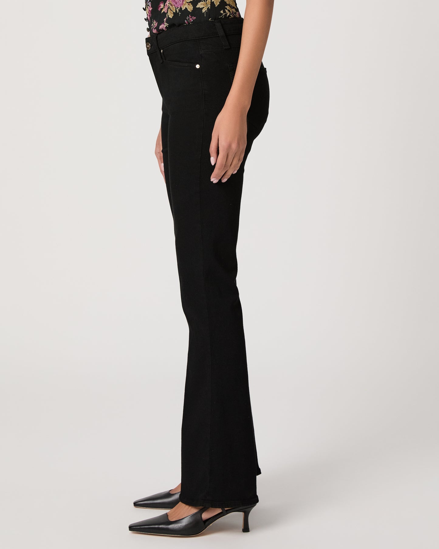 Woman wearing a floral to, black pants, and black heels on a white background