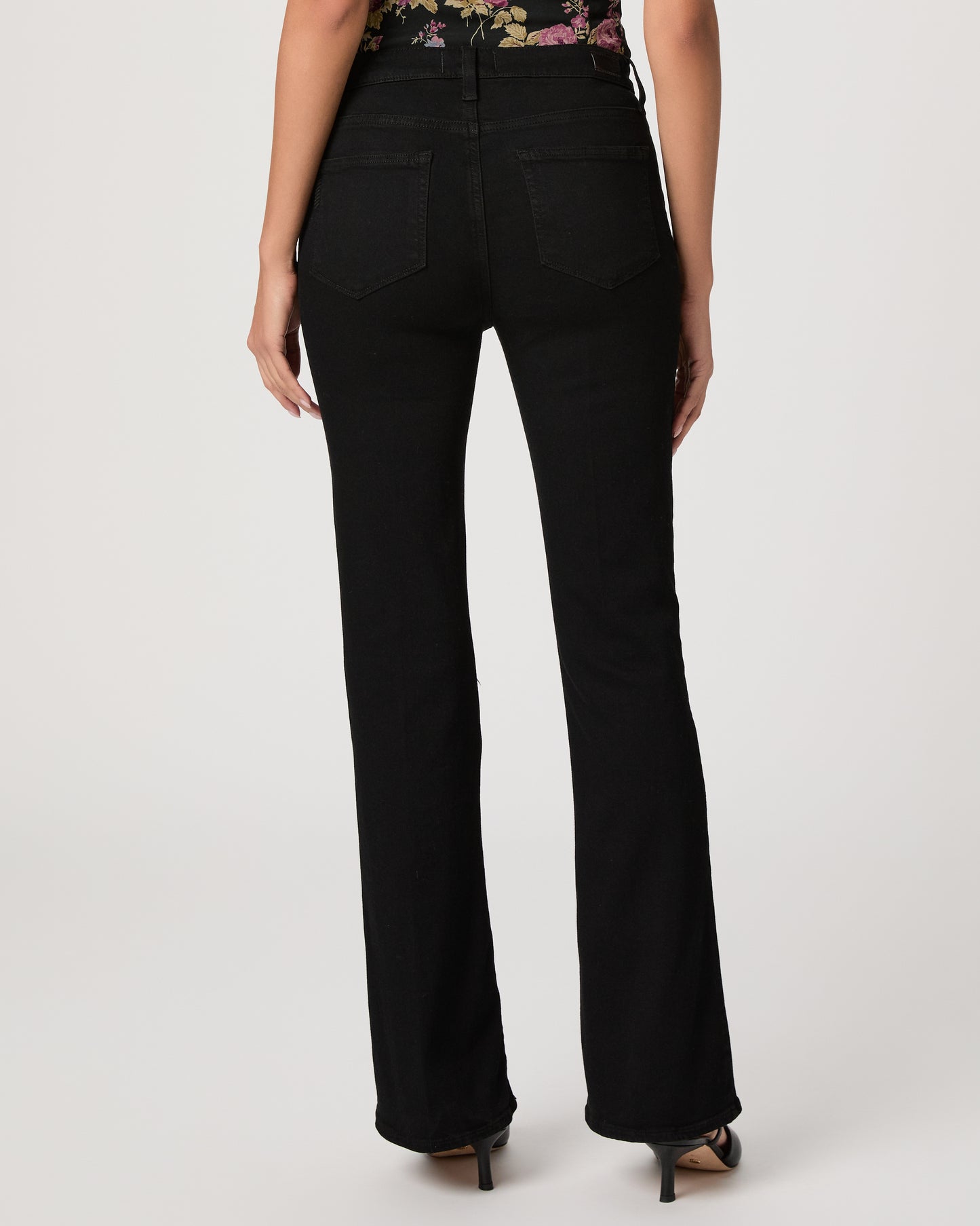 Woman wearing a floral to, black pants, and black heels on a white background