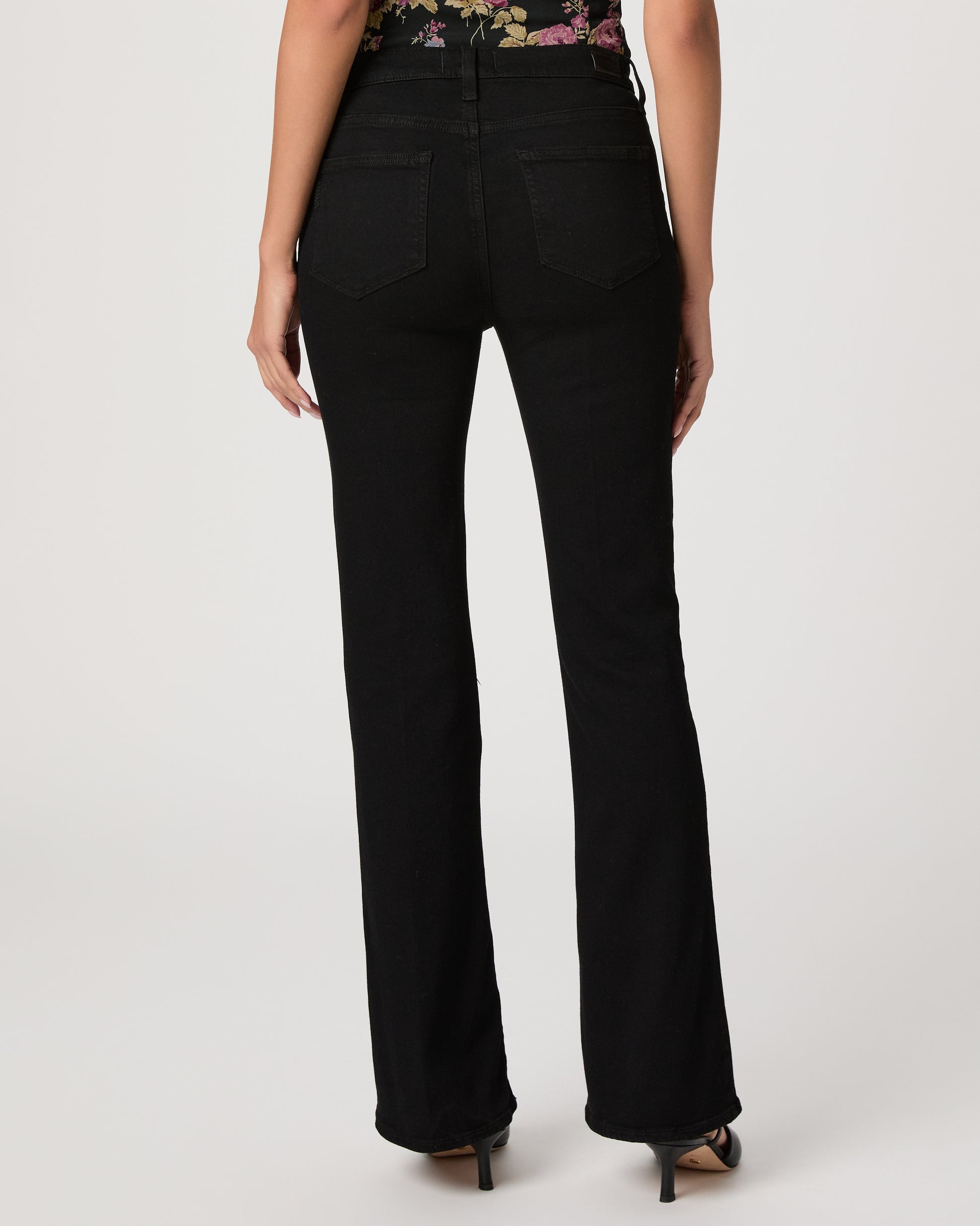 Woman wearing a floral to, black pants, and black heels on a white background