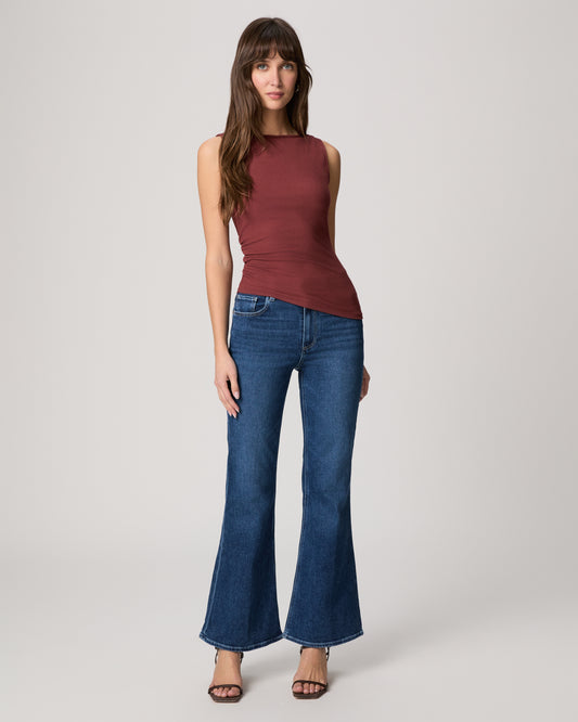 Woman wearing a sleeveless burgundy top and blue jeans on a white background