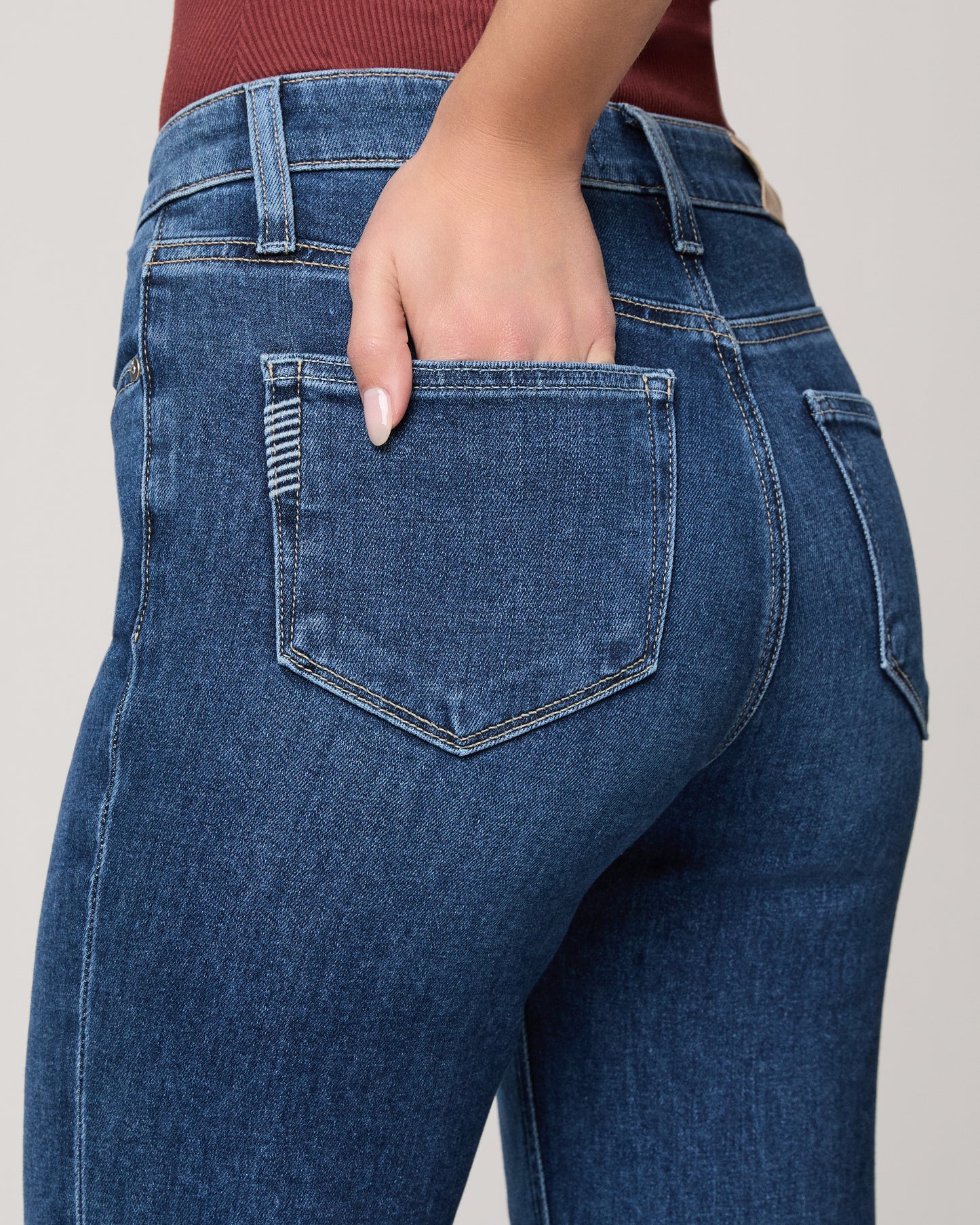 Close-up of blue jeans with a hand in the pocket on a neutral background