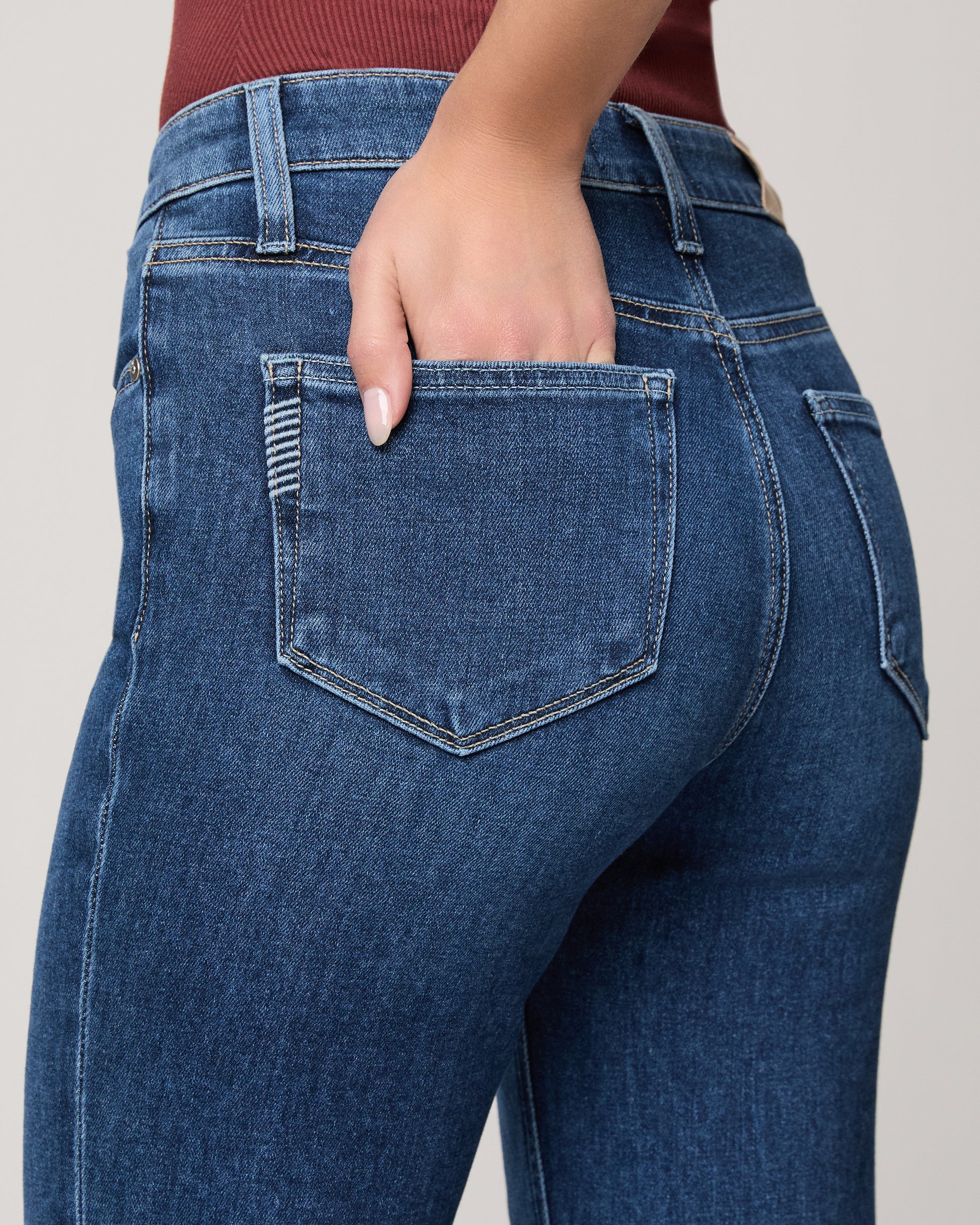 Close-up of blue jeans with a hand in the pocket on a neutral background