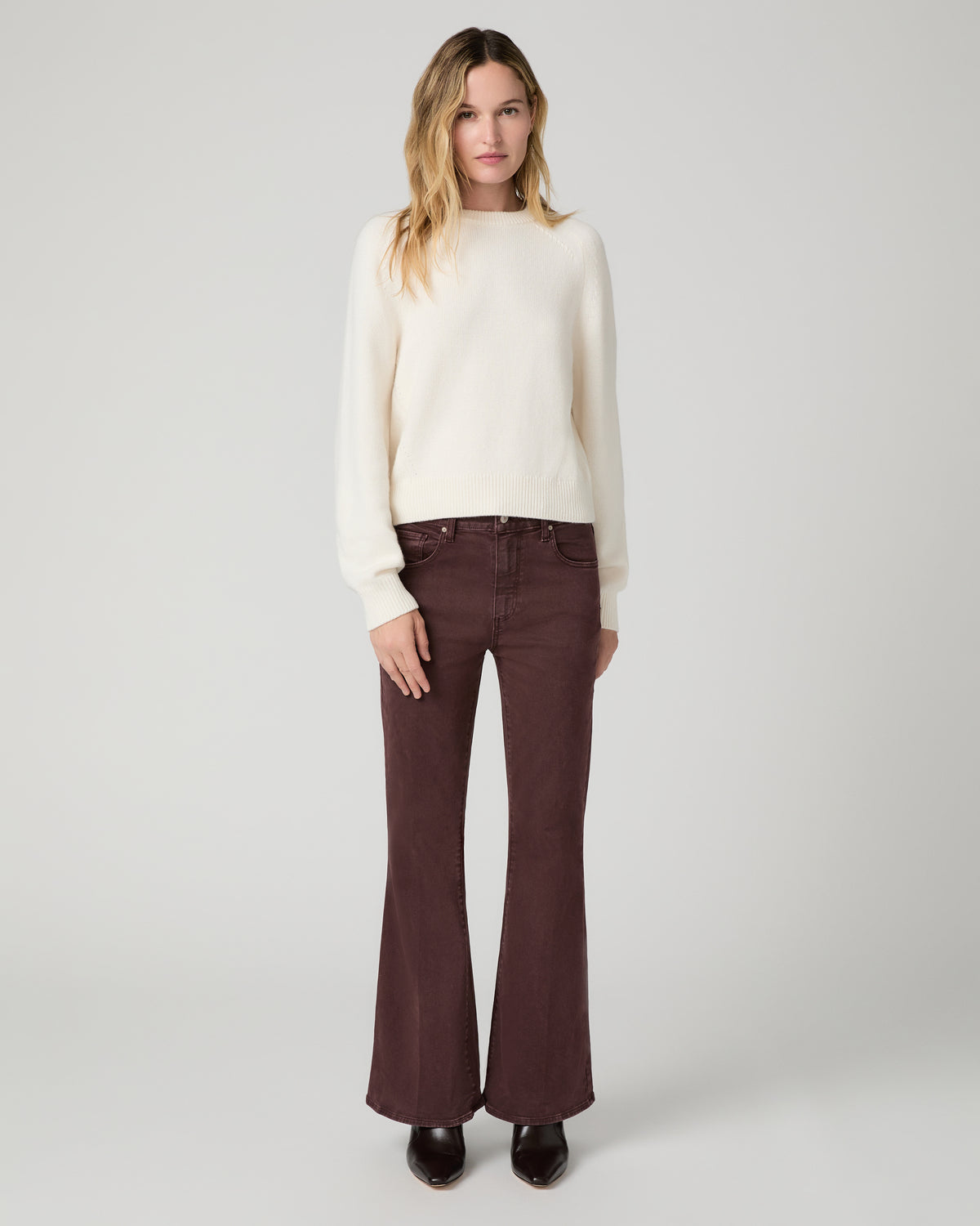 Women wearing a white top paired with burgundy jean and brown boots against a white background