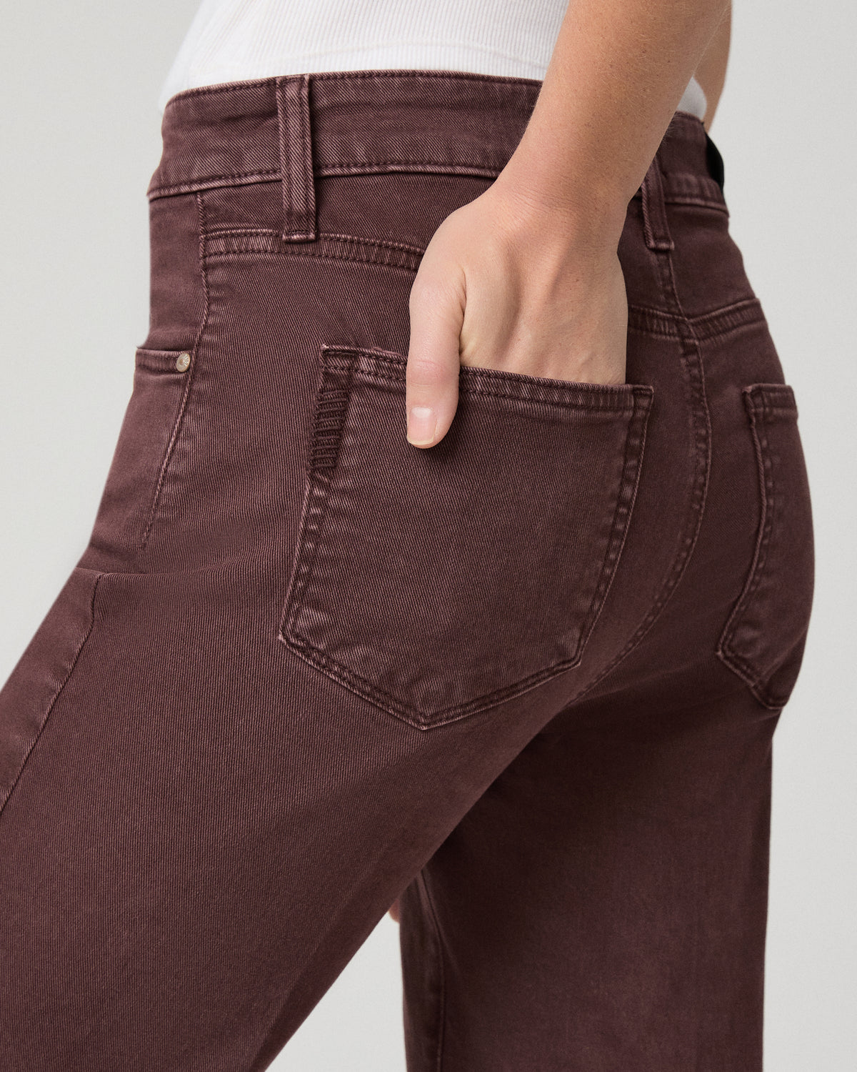 Women wearing a white top paired with burgundy jean and brown boots against a white background