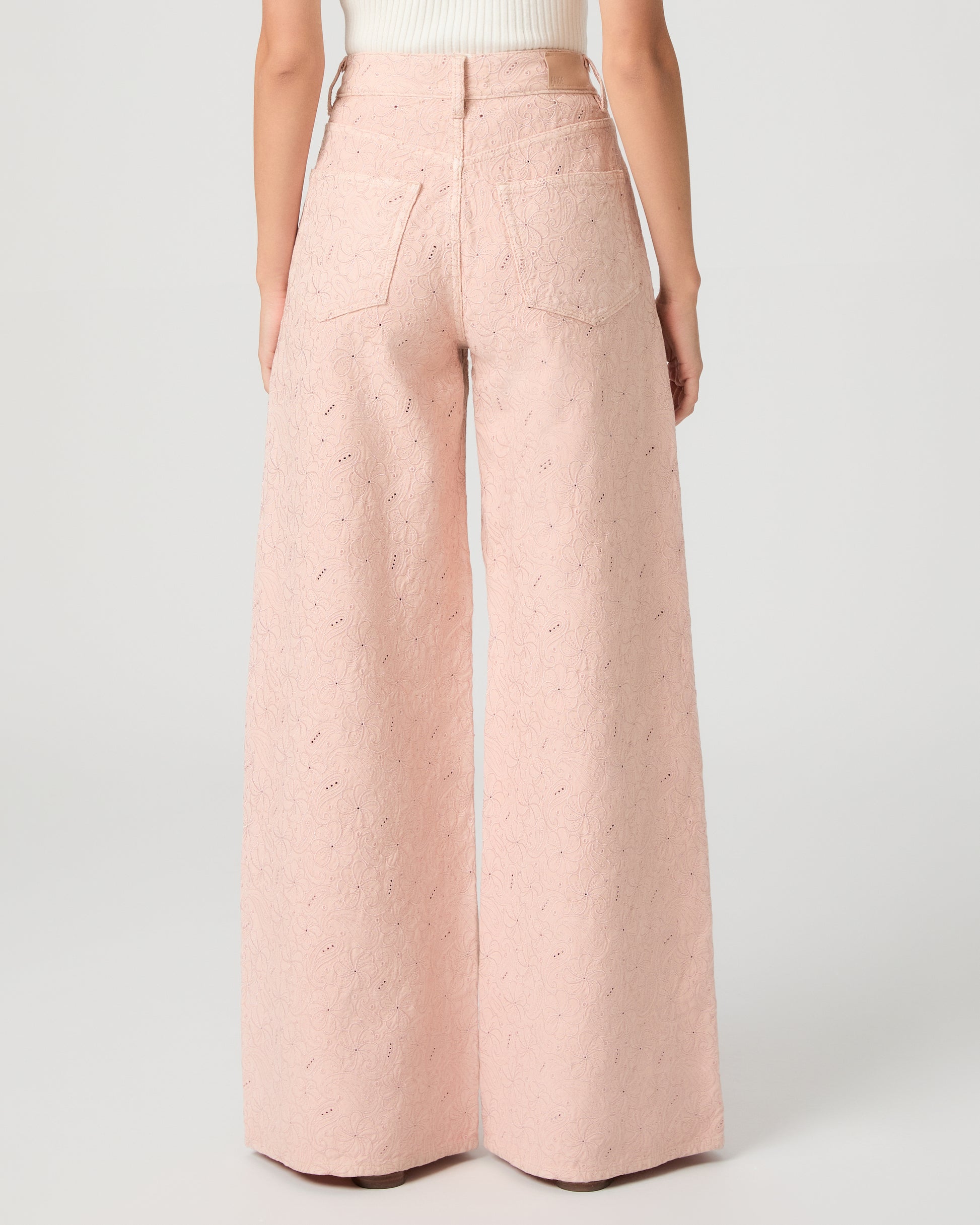 Woman wearing a white sleeveless top and pink wide-leg pants on a white background