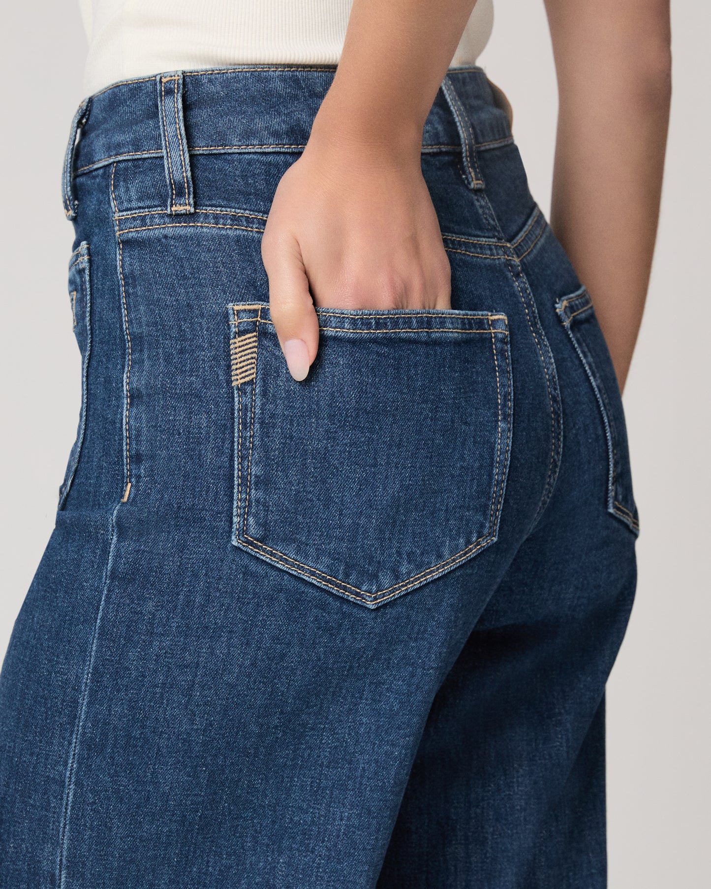 Woman wearing a white top and blue jeans paired with brown flats on a plain background