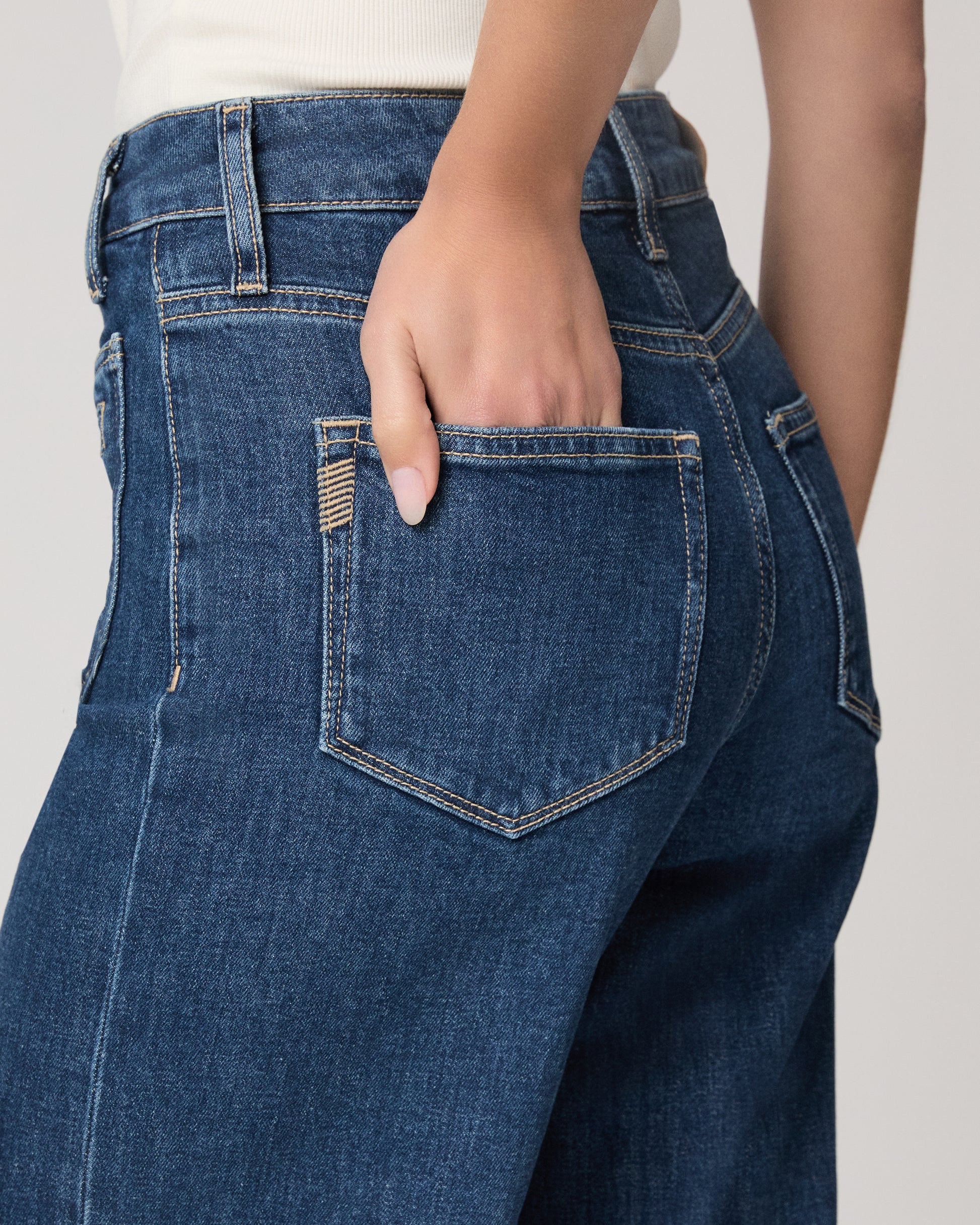 Woman wearing a white top and blue jeans paired with brown flats on a plain background