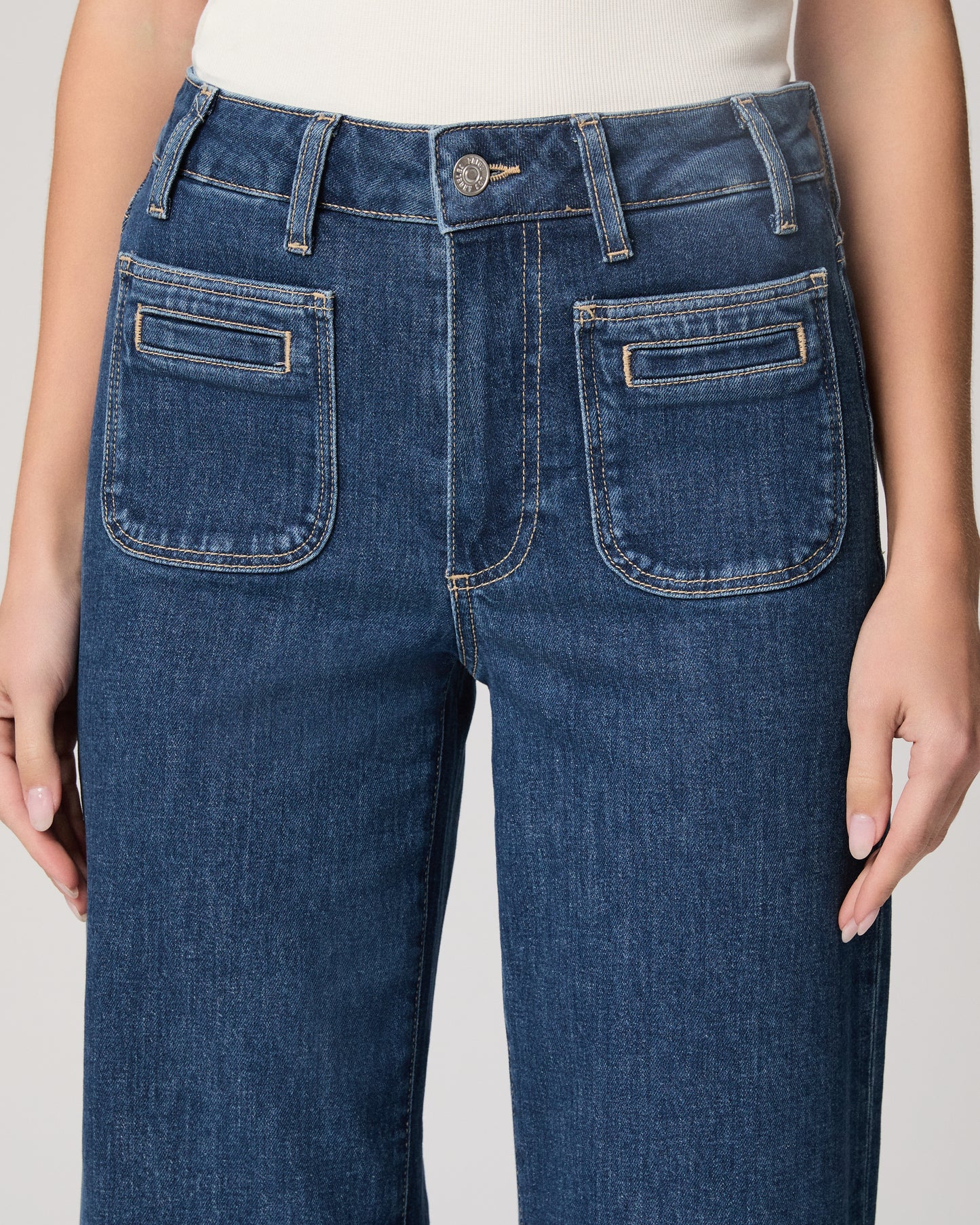 Woman wearing a white top and blue jeans paired on a plain background