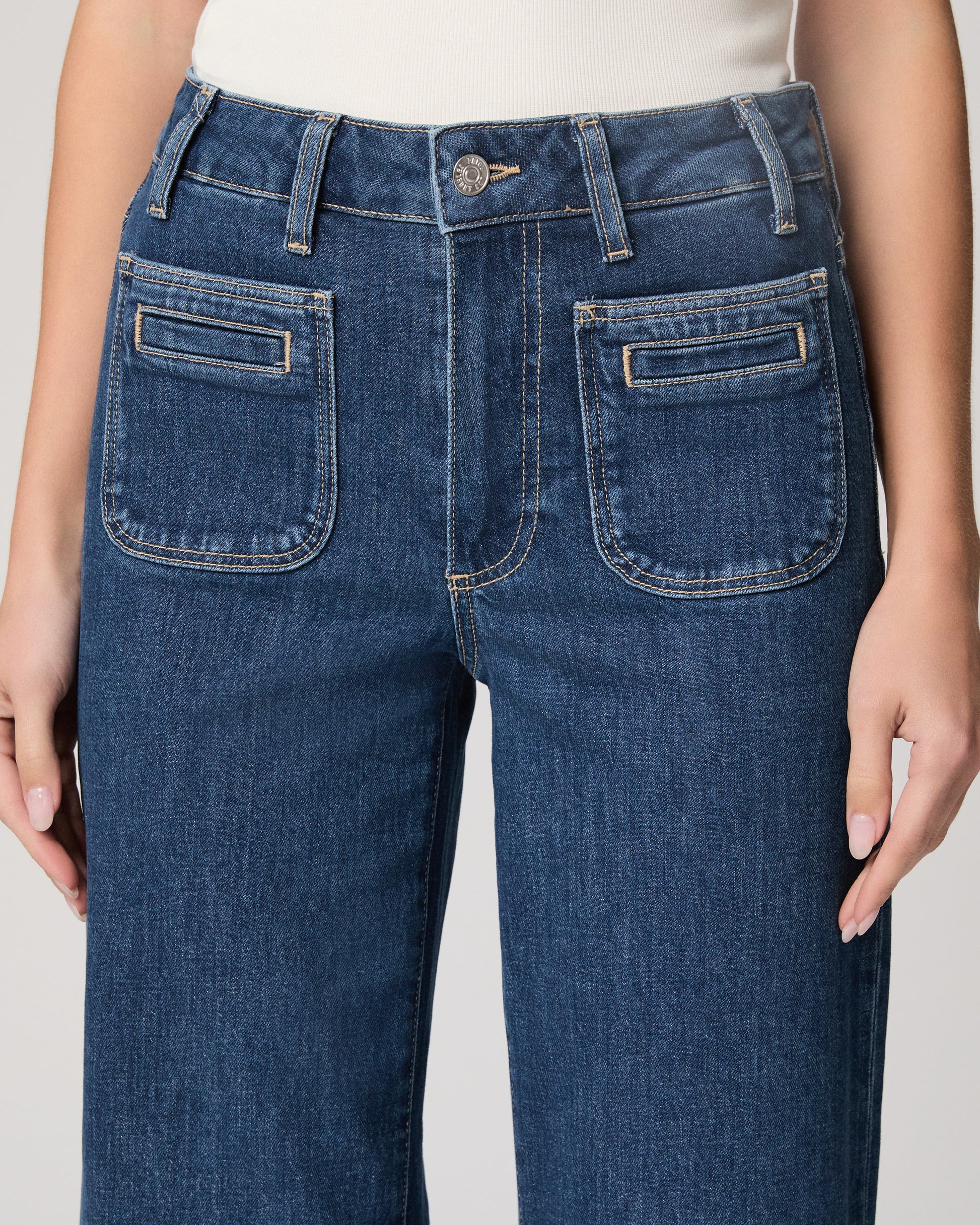 Woman wearing a white top and blue jeans paired on a plain background
