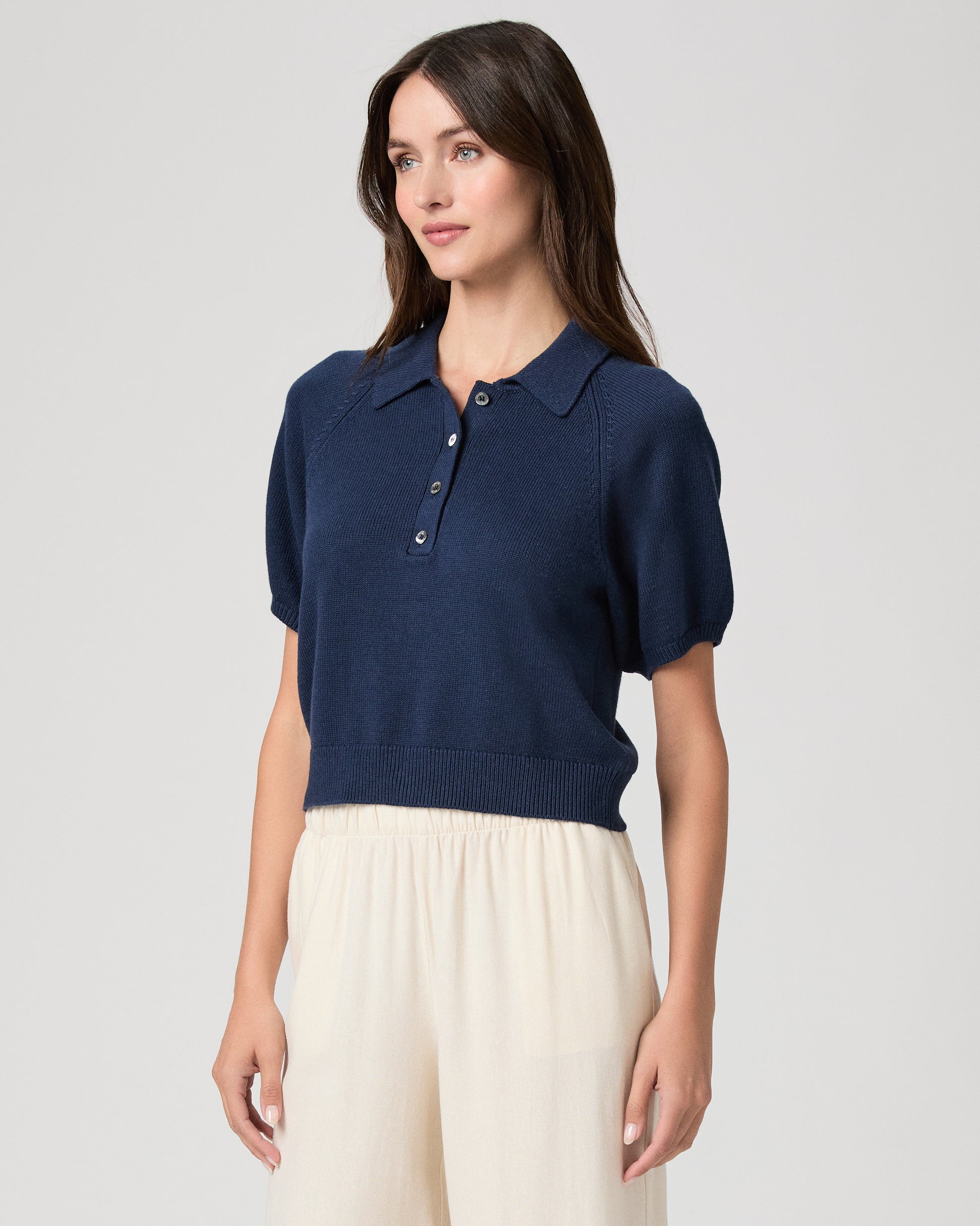 Woman wearing a navy blue polo shirt and white pants on a light gray background