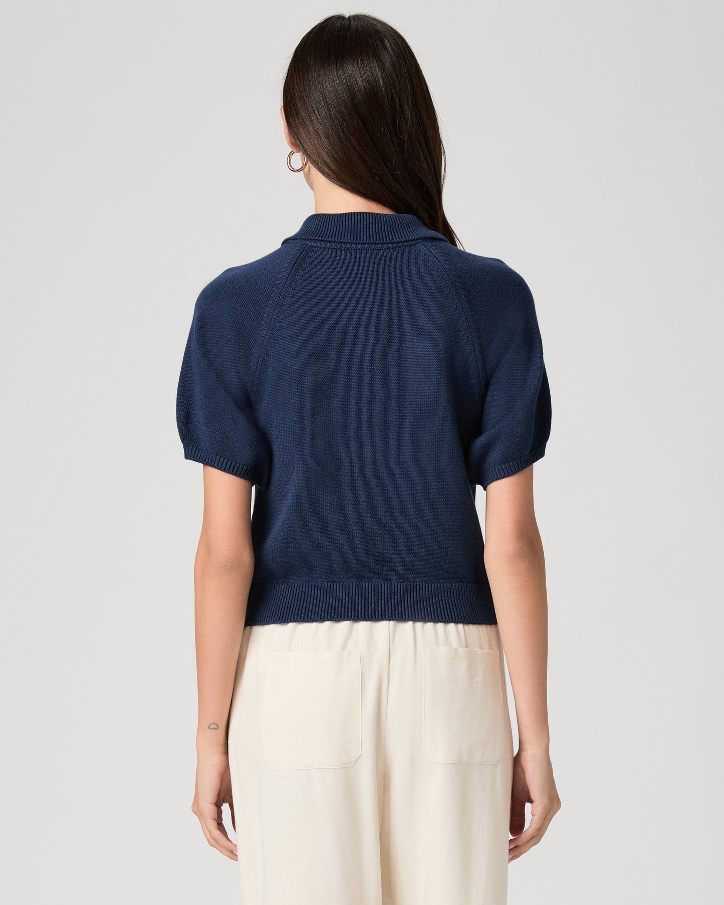Woman wearing a navy blue polo shirt and white pants on a light gray background