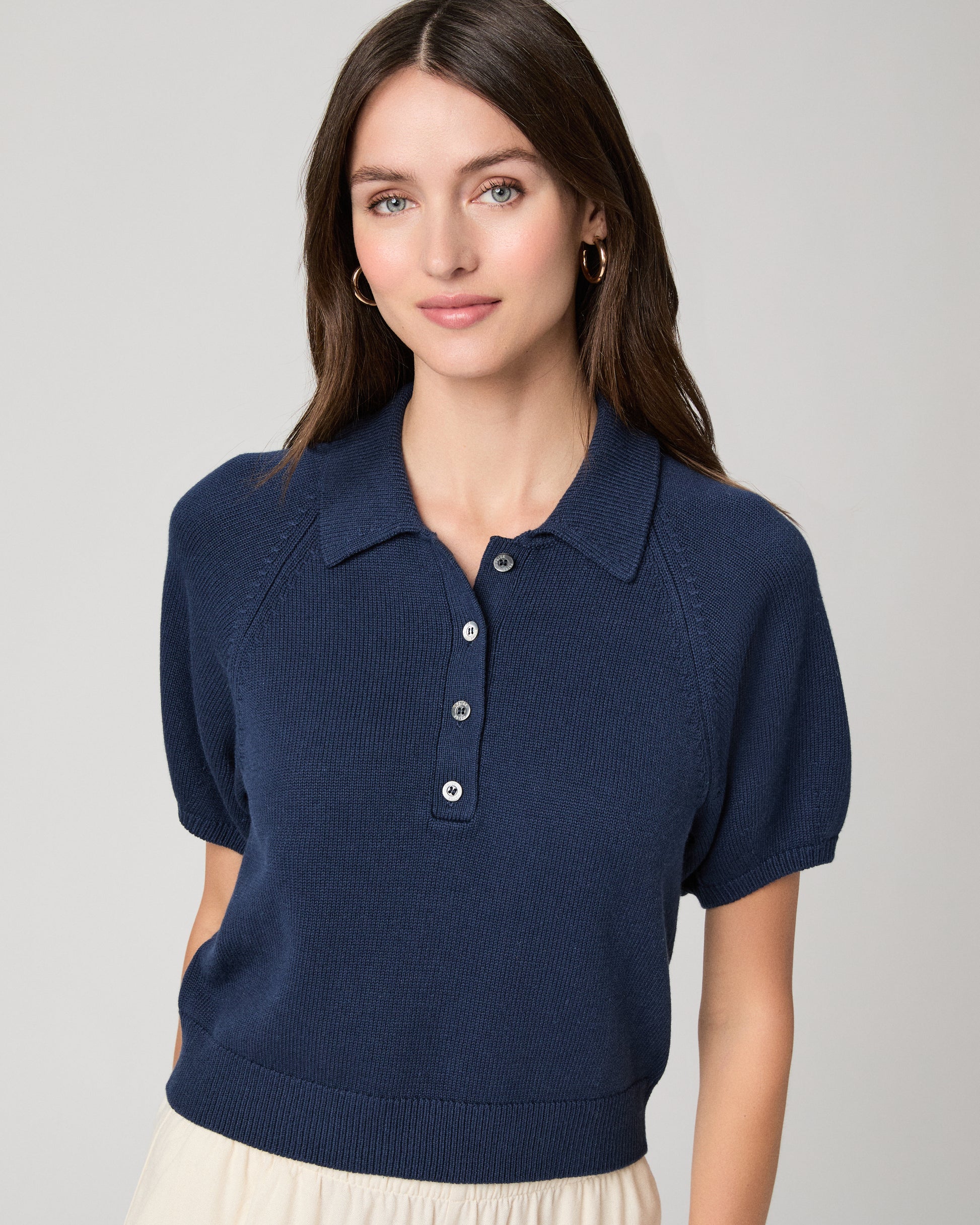 Woman wearing a navy blue polo shirt and white pants on a light gray background