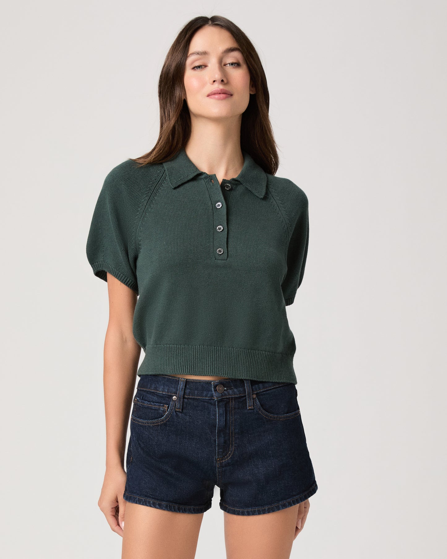 Model wearing green short sleeve sweater top paired with dark wash denim shorts