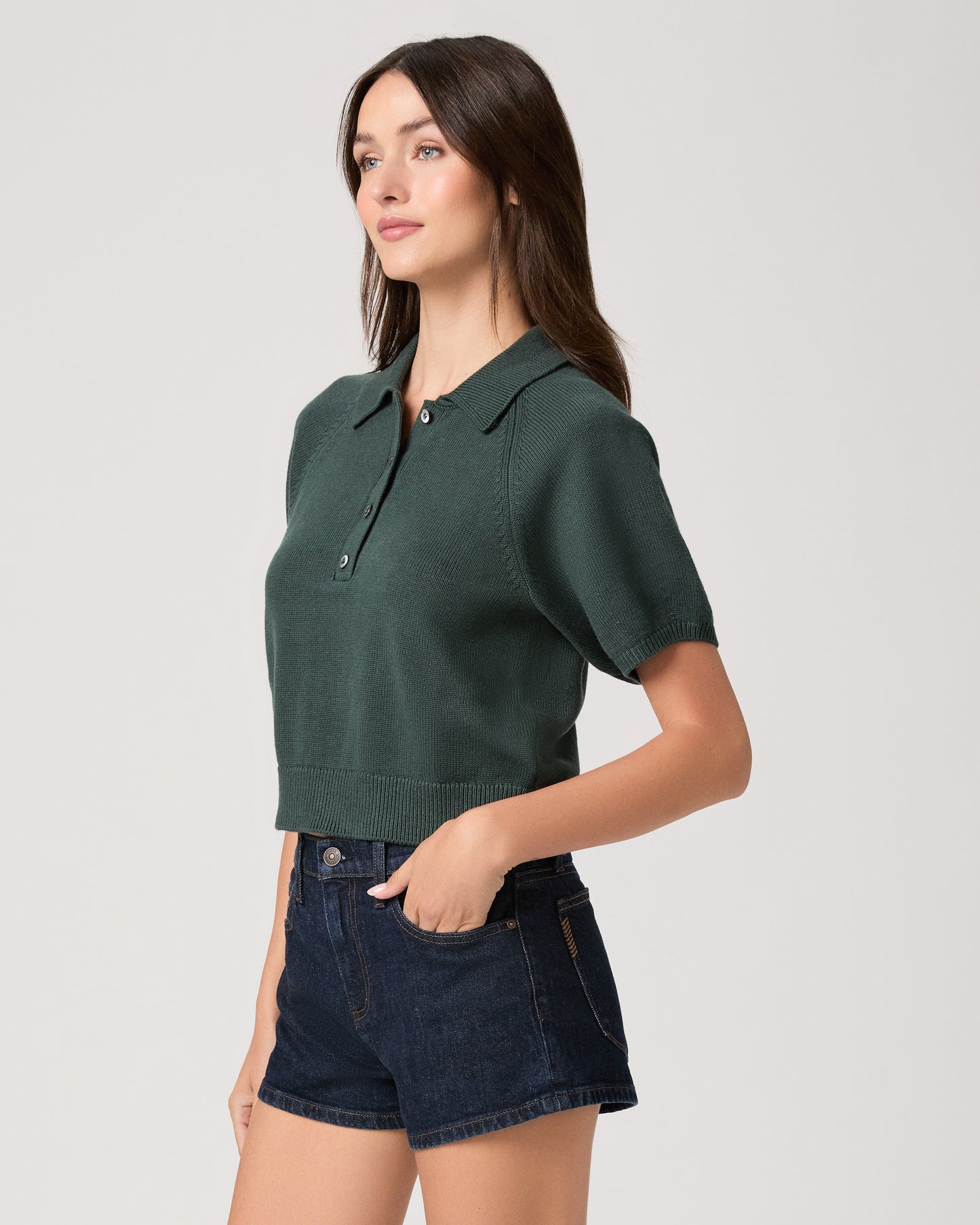Model wearing green short sleeve sweater top paired with dark wash denim shorts