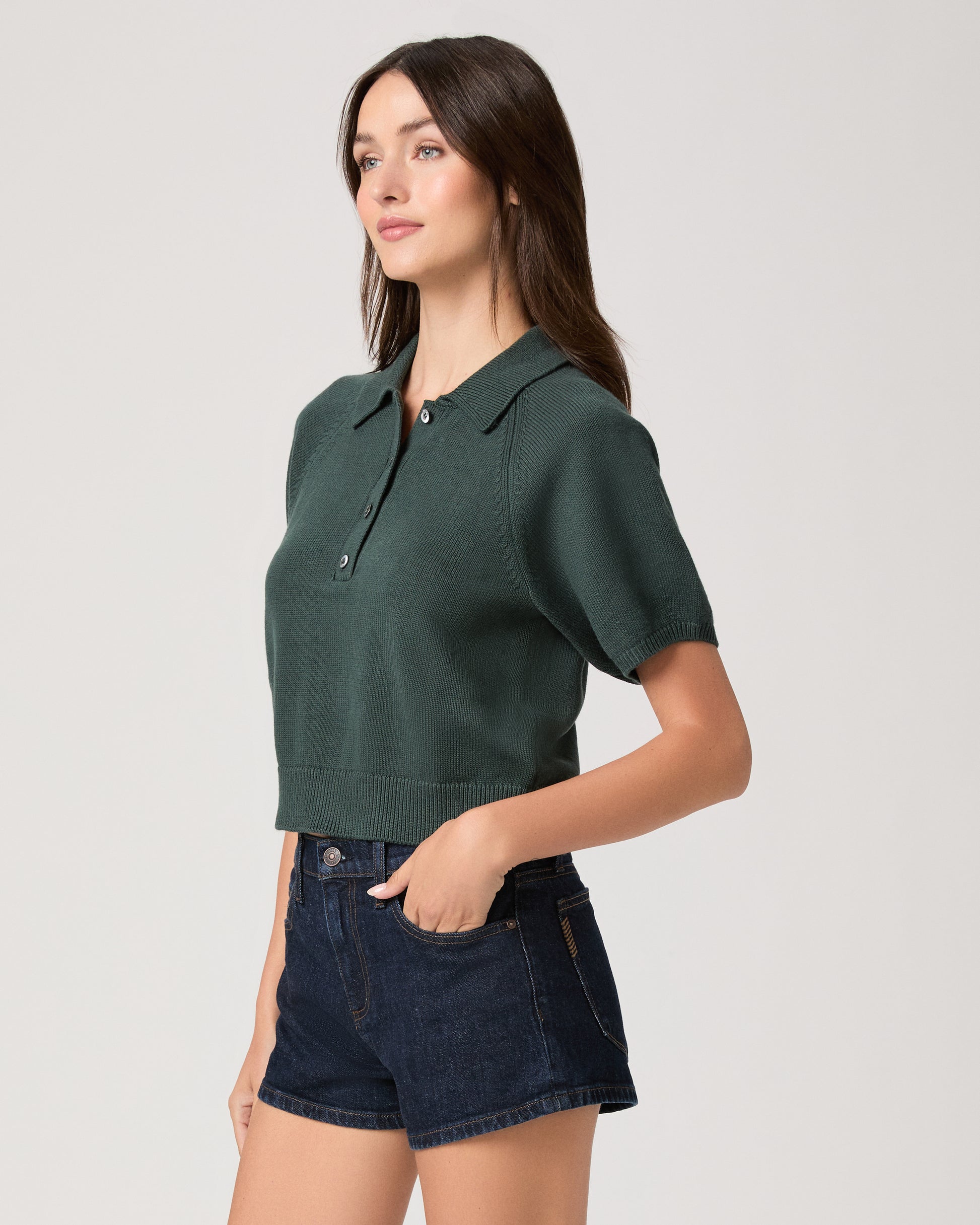Model wearing green short sleeve sweater top paired with dark wash denim shorts