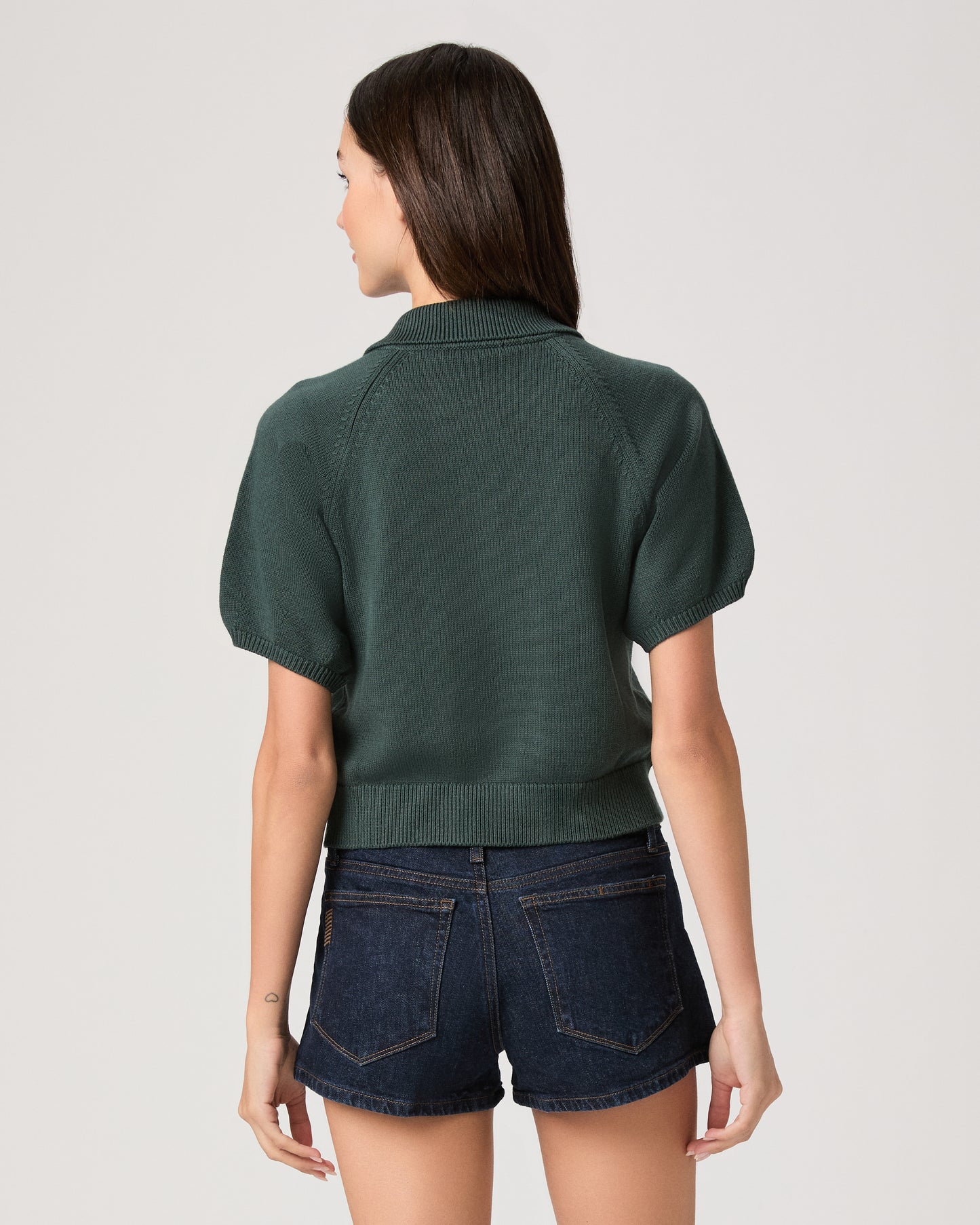 Model wearing green short sleeve sweater top paired with dark wash denim shorts