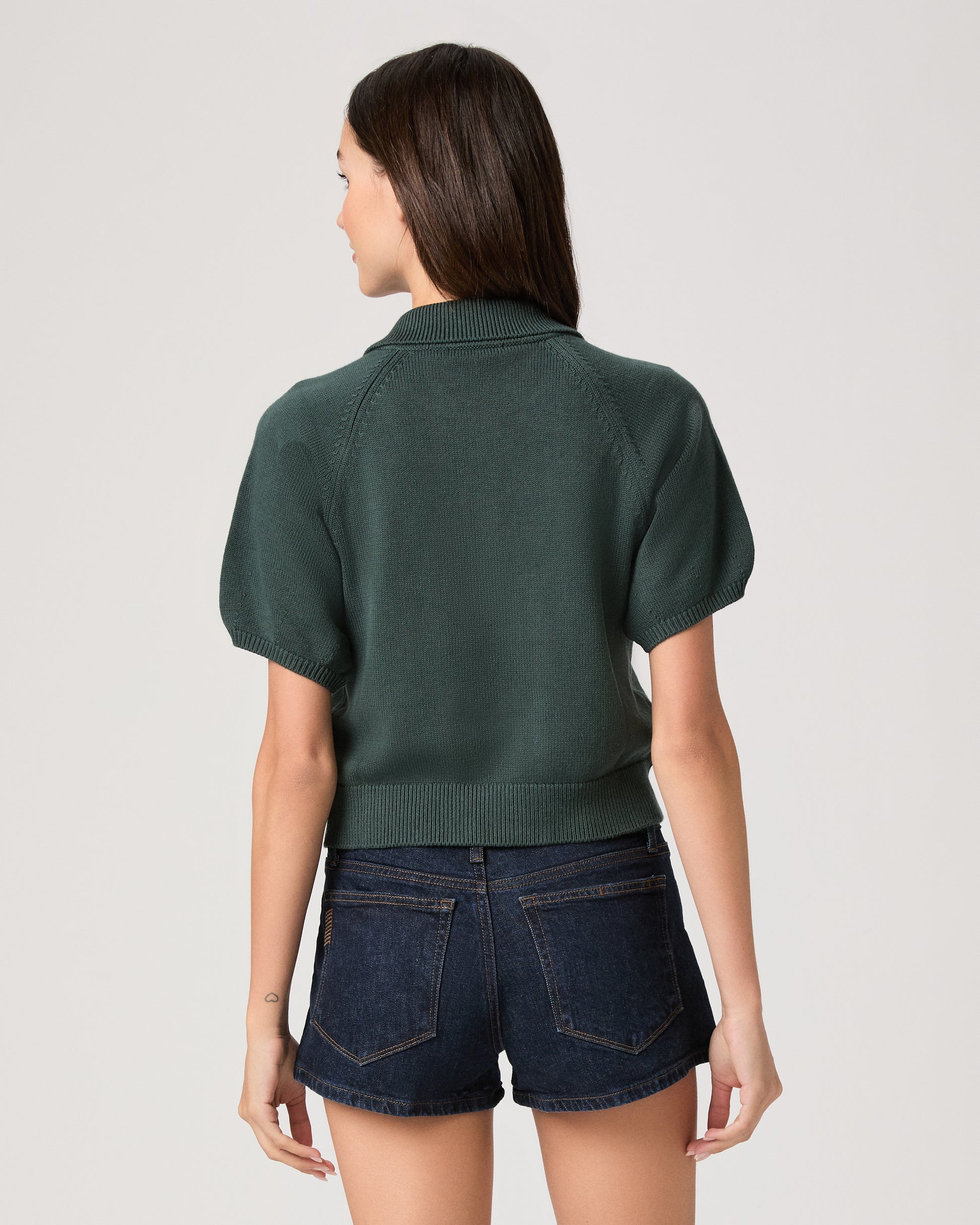 Model wearing green short sleeve sweater top paired with dark wash denim shorts